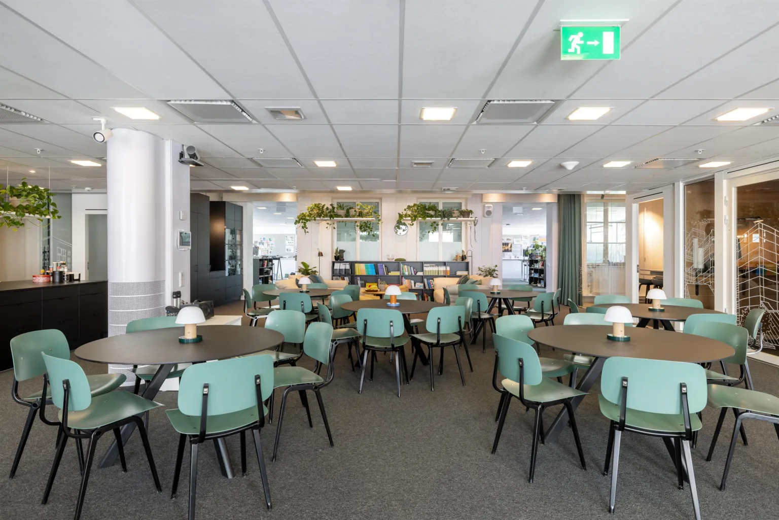 3. En matsal med flera runda bord och mintgröna stolar, inredd med växter och moderna belysningsdetaljer.