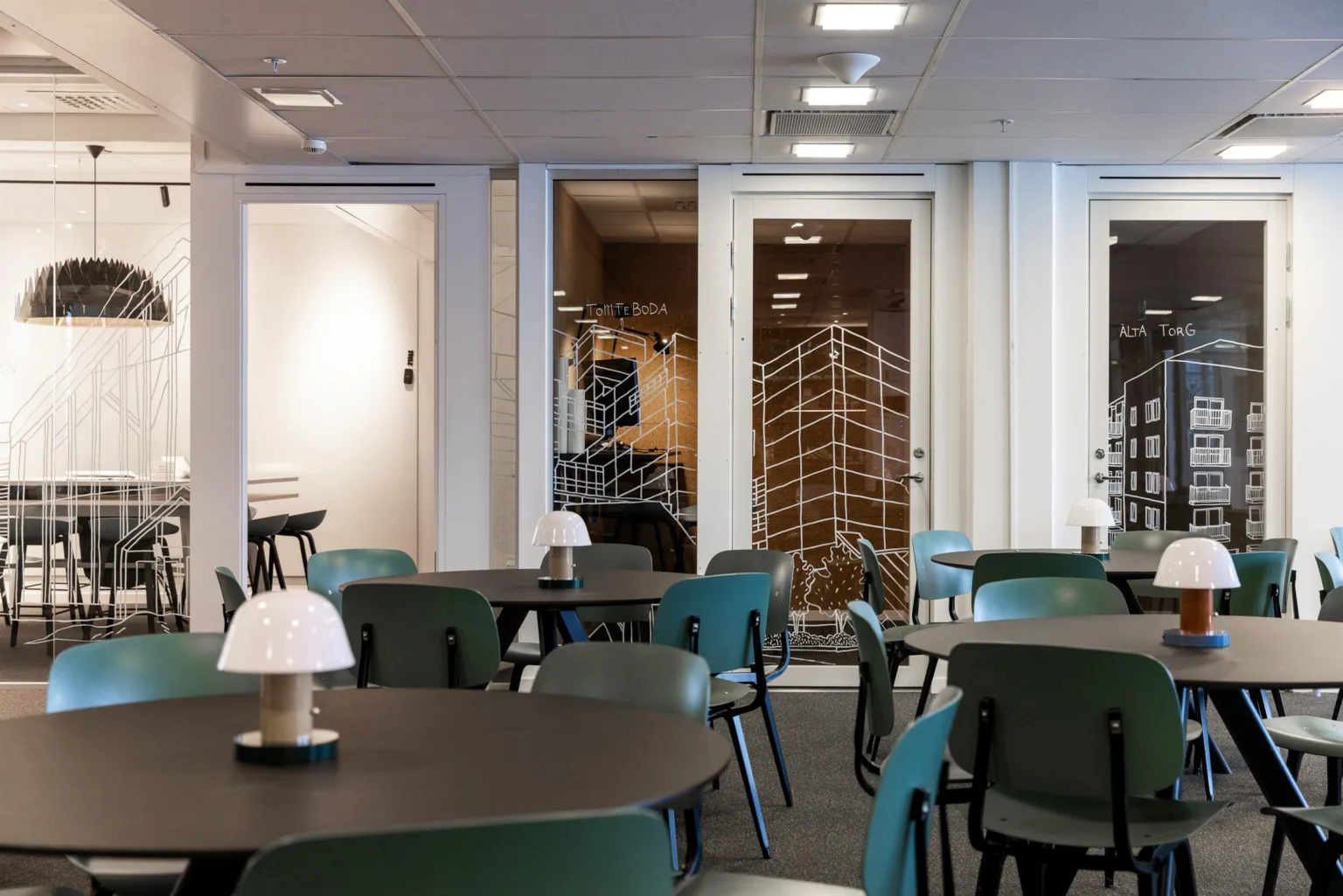 1. Ett modernt kaféområde med runda bord, gröna stolar och dekorativa glasväggar i bakgrunden.