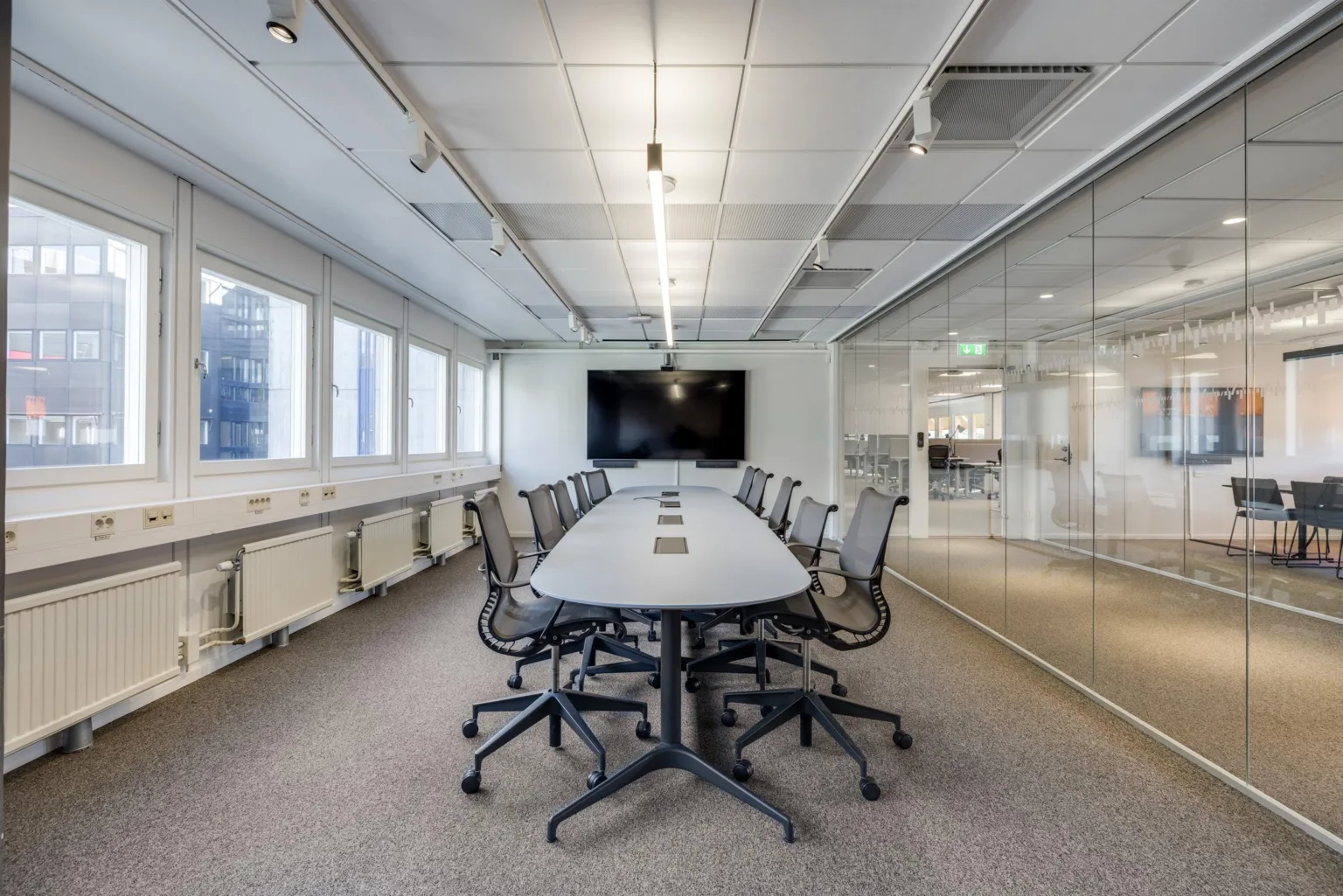 1. Ett modernt konferensrum med långbord, stolar och en stor skärm på väggen, omgiven av glasväggar och stora fönster.