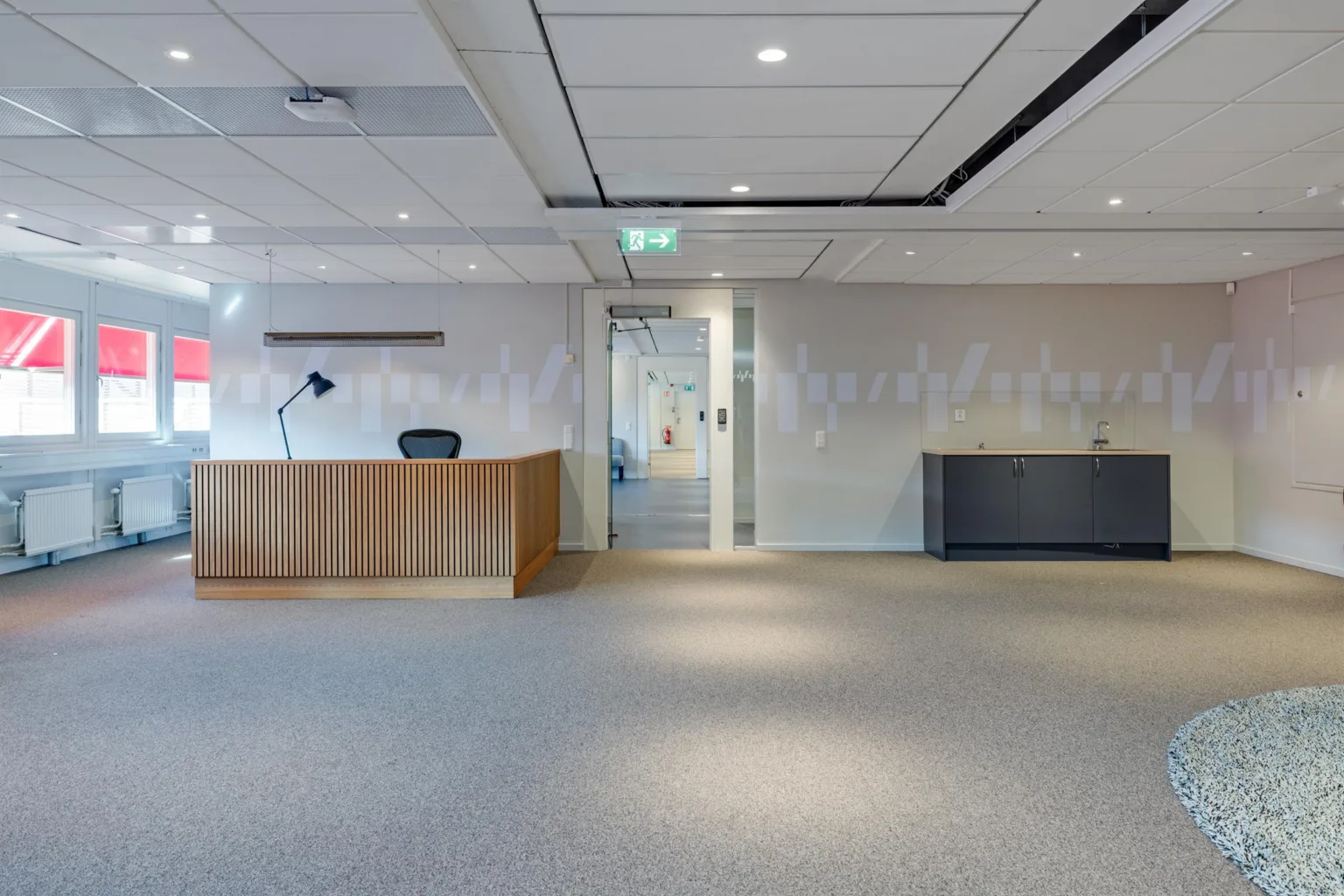 Reception med trädisk, skrivbordslampa och en glasdörr i bakgrunden.