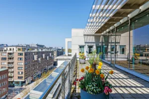5. Balkong med färgglada blommor i krukor, med utsikt över en stadsmiljö under en klar blå himmel.