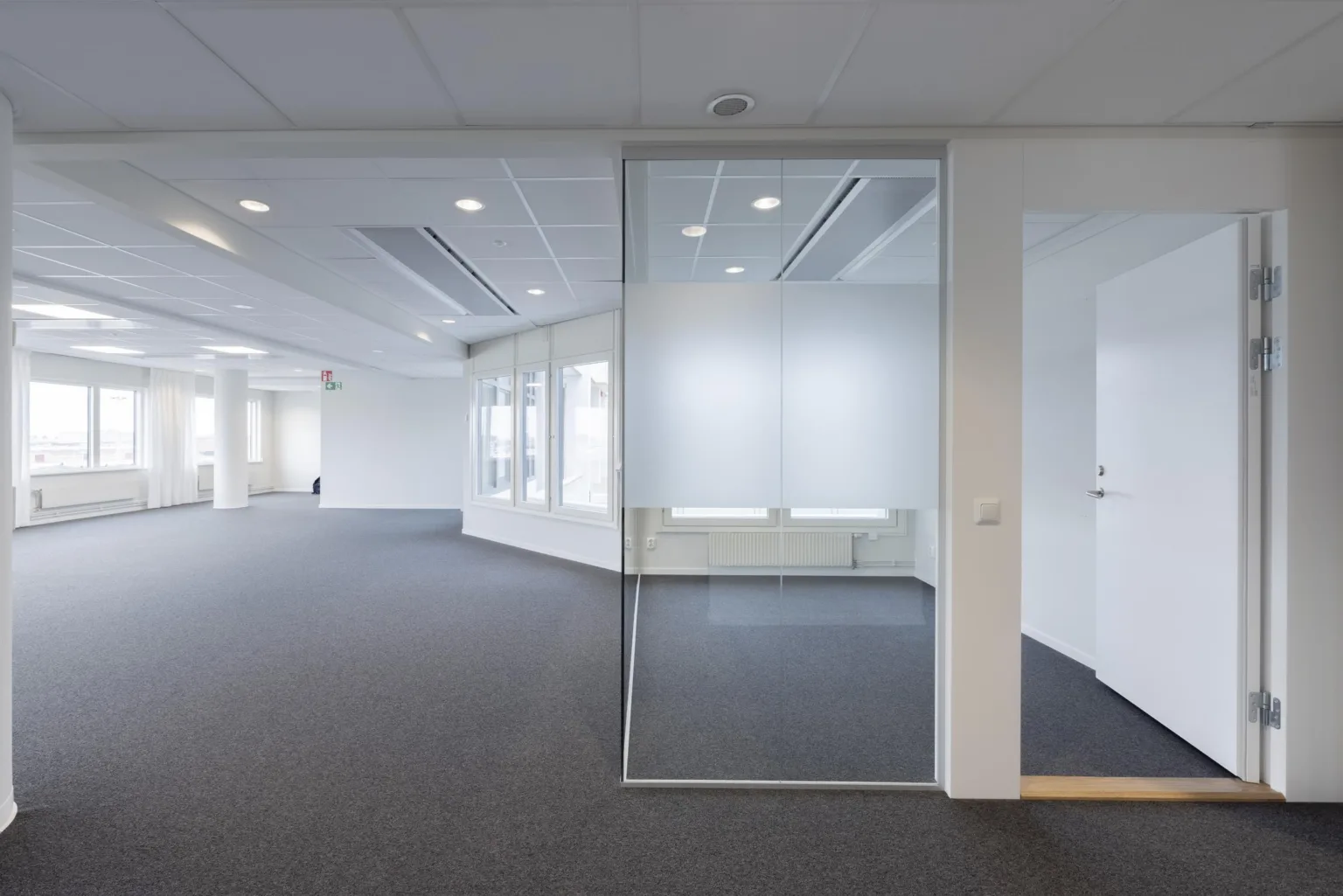 3. En ljus kontorsmiljö med glasväggar och grå heltäckningsmatta.