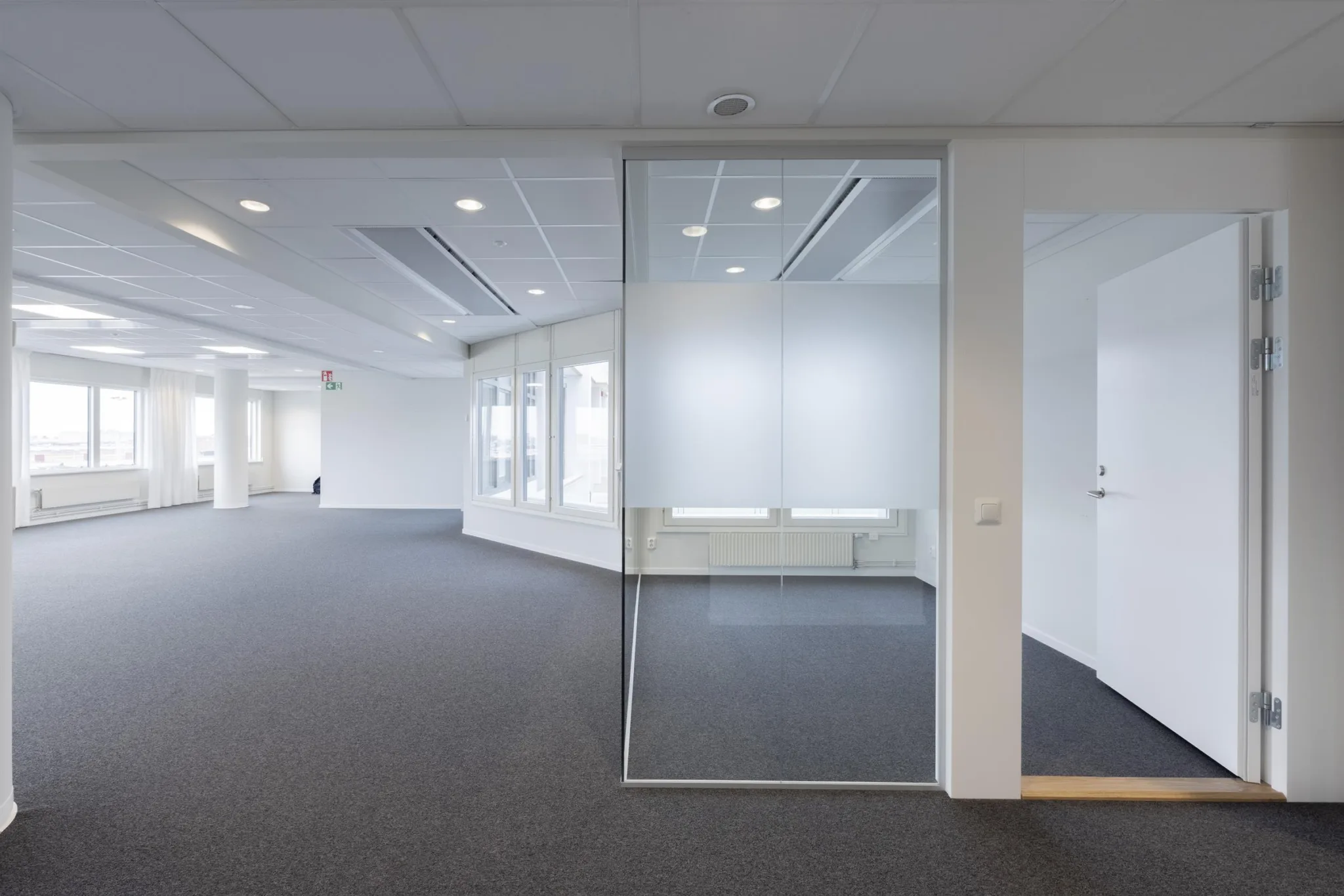 3. En ljus kontorsmiljö med glasväggar och grå heltäckningsmatta.