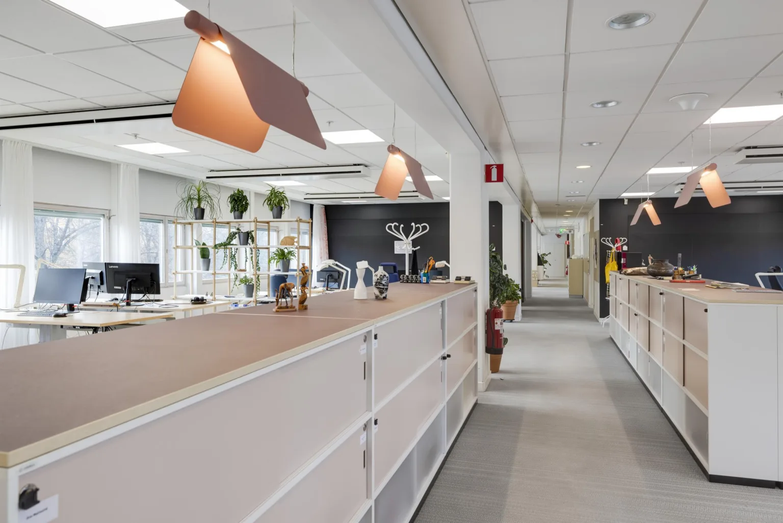 En ljus kontorsmiljö med skrivbord, växter och moderna lampor.