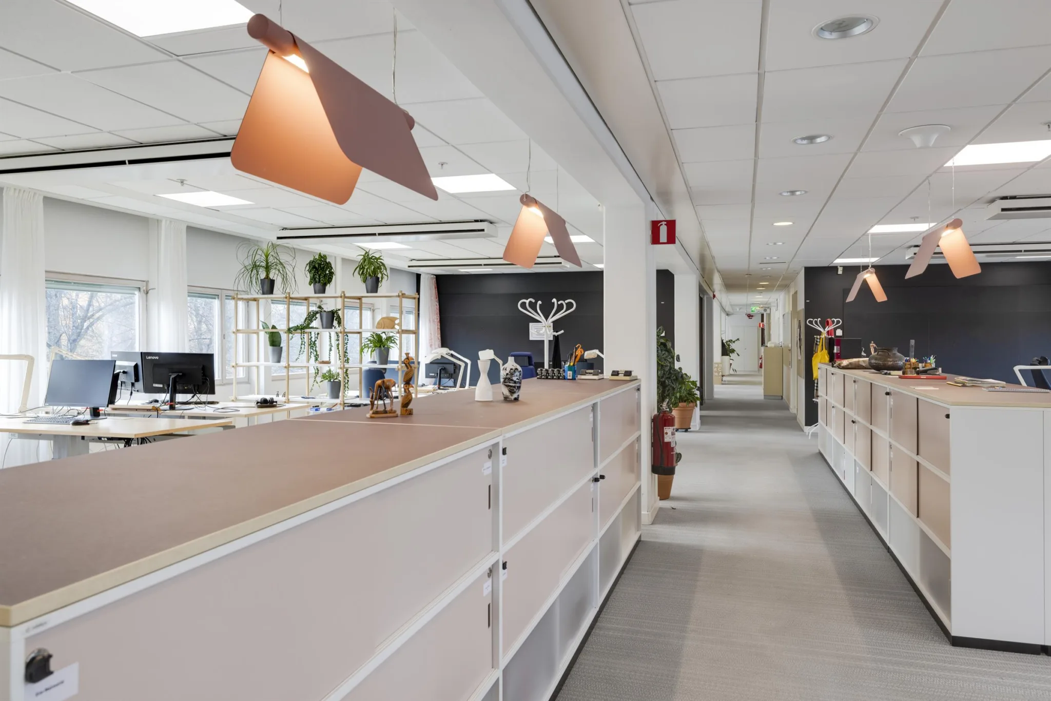 En ljus kontorsmiljö med skrivbord, växter och moderna lampor.
