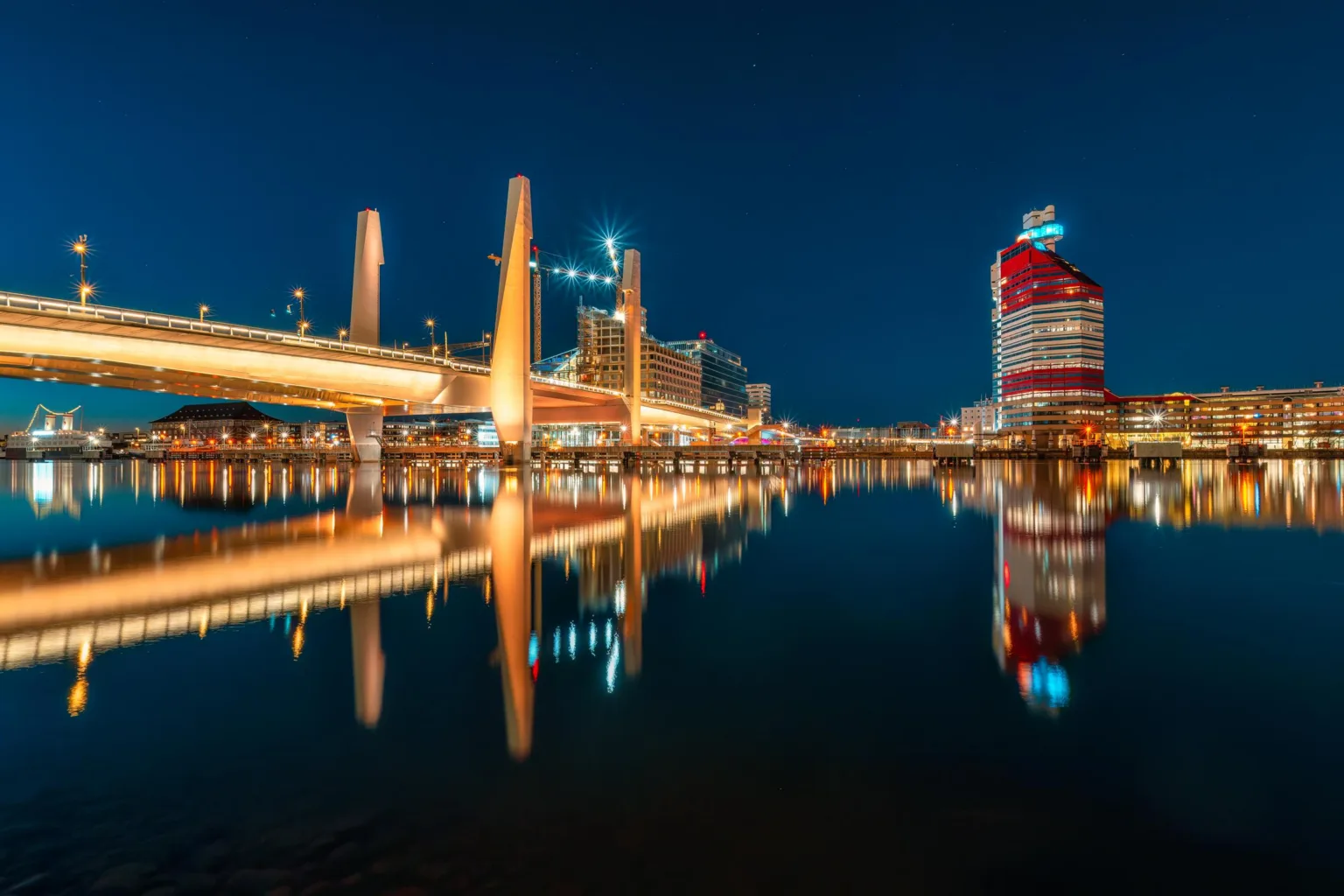 En nattlig vy av en stad med upplysta broar och byggnader reflekterade i vattnet.
