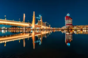 En nattlig vy av en stad med upplysta broar och byggnader reflekterade i vattnet.