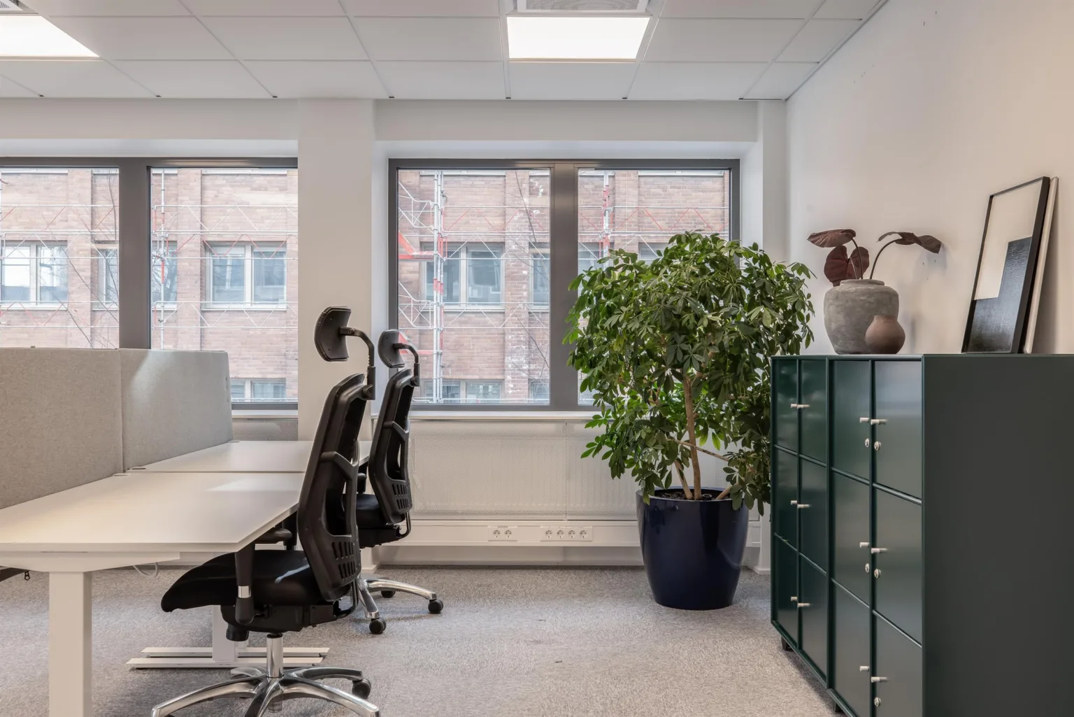 2. Modernt kontor med skrivbord, svarta stolar, stora fönster och en grön växt.