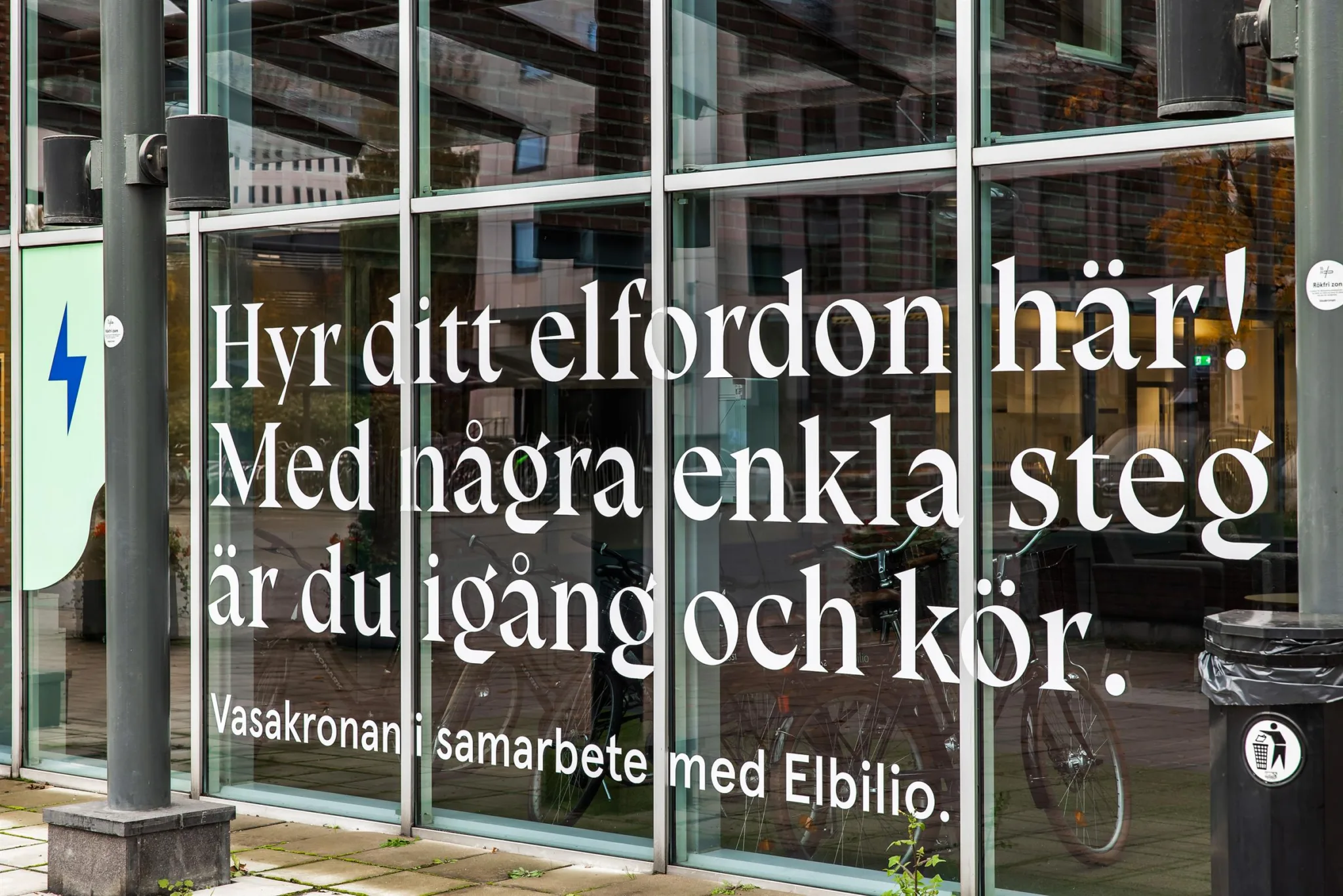 Skyltfönster med texten: "Hyr ditt elfordon här. Med några enkla steg är du igång och kör. I samarbete med Elbilio."