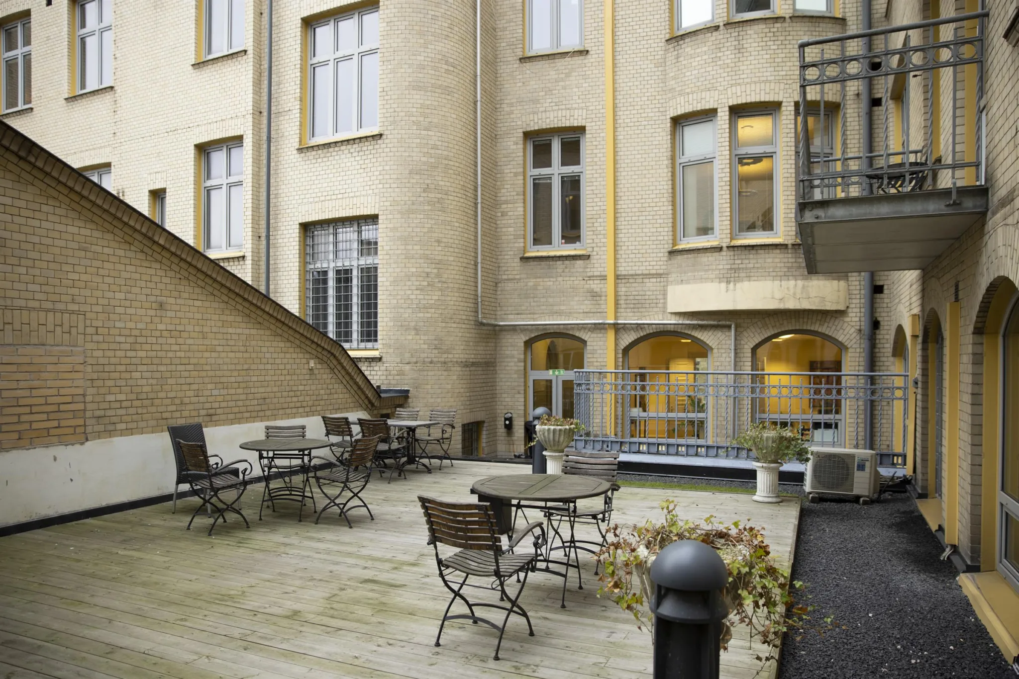 En innergård med träbord, stolar och omgivande ljusgula fasader med stora fönster.