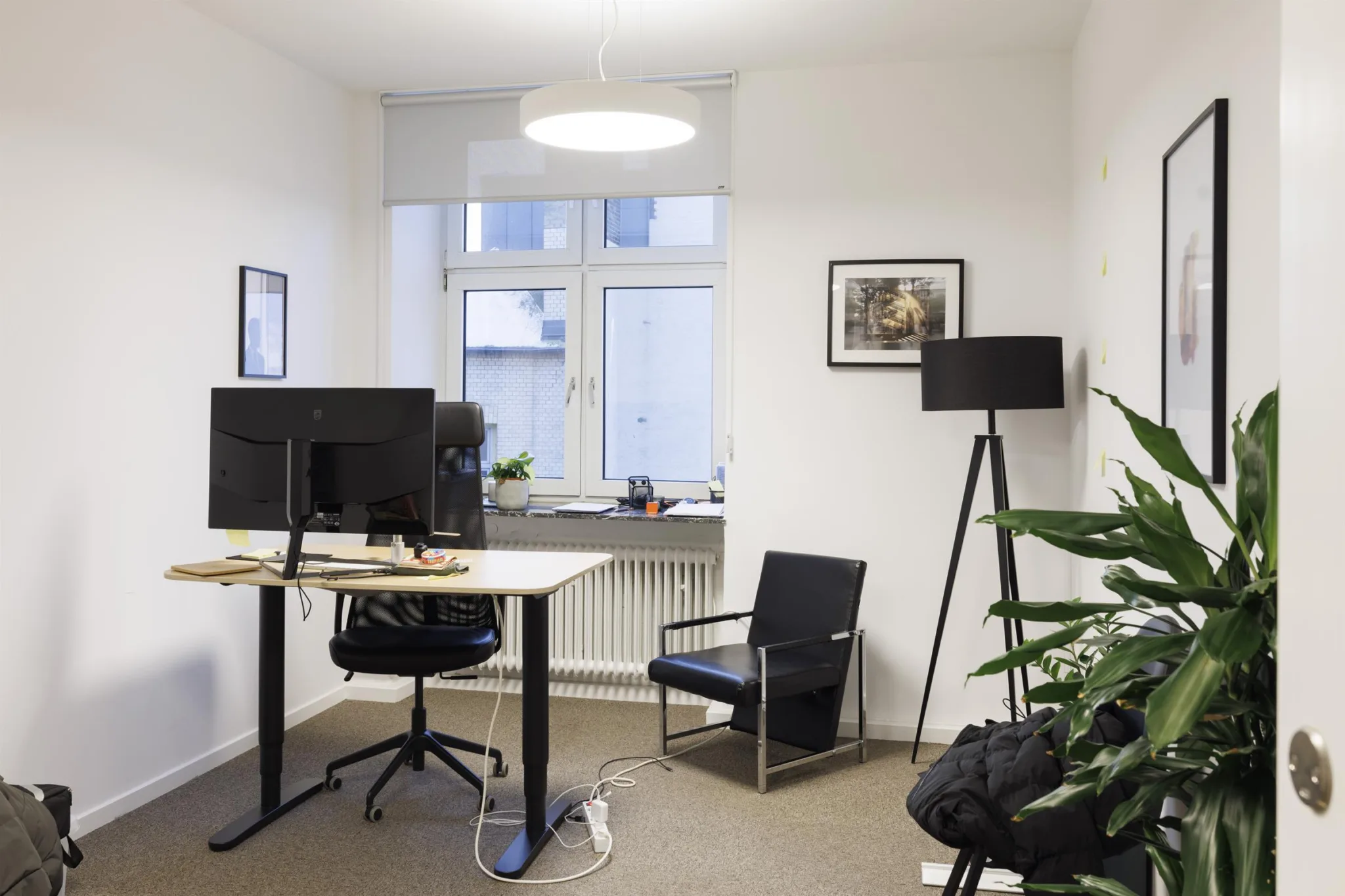 Ett ljust kontor med skrivbord, stol, växter och en golvlampa.