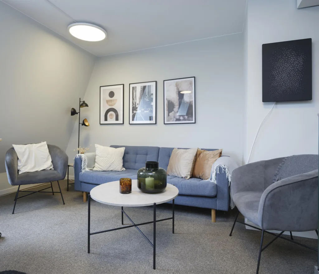 Ett vardagsrum med en blå soffa, fåtöljer, ett runt soffbord och väggdekorationer.