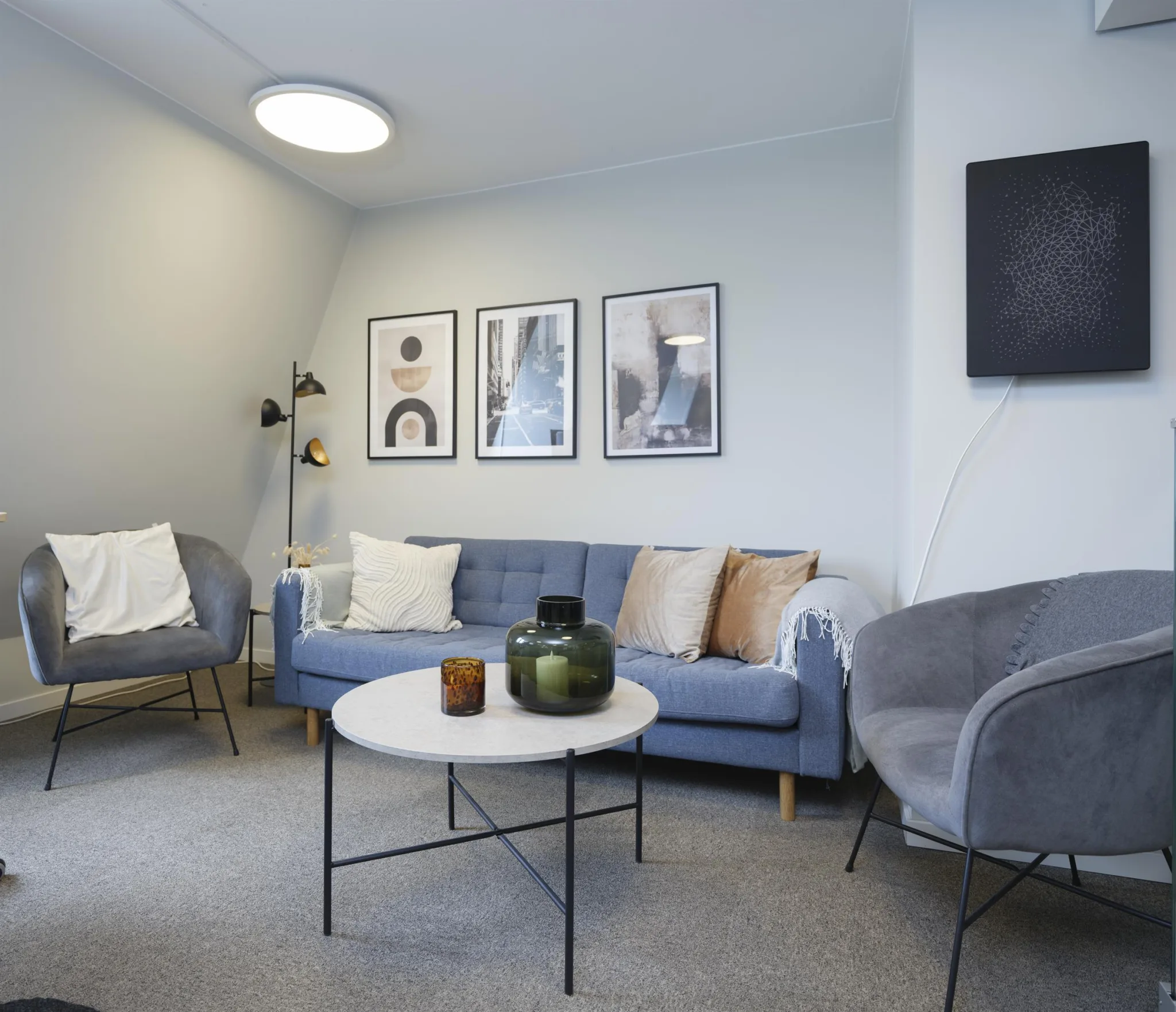 Ett vardagsrum med en blå soffa, fåtöljer, ett runt soffbord och väggdekorationer.