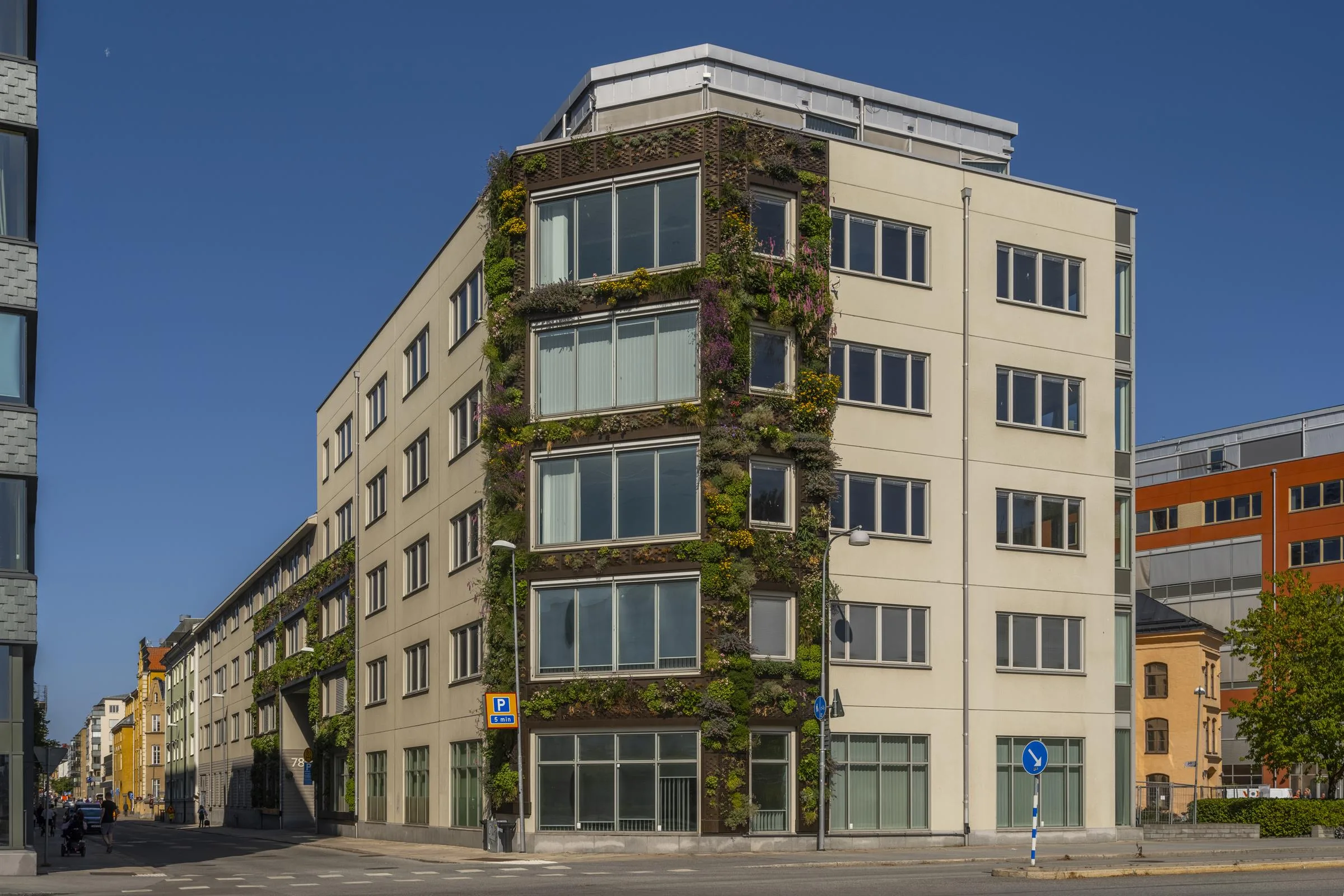 En modern byggnad med växtväggar och stora fönster under en klar himmel.