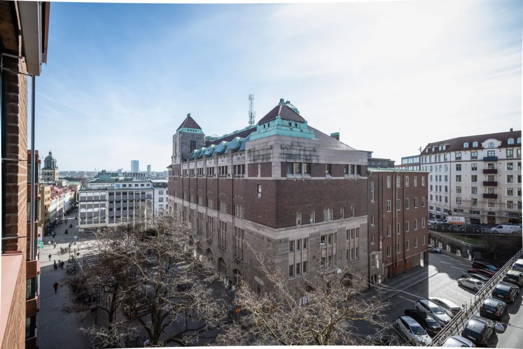 En stor byggnad i sten med gröna takdetaljer, omgiven av stadsmiljö och träd.