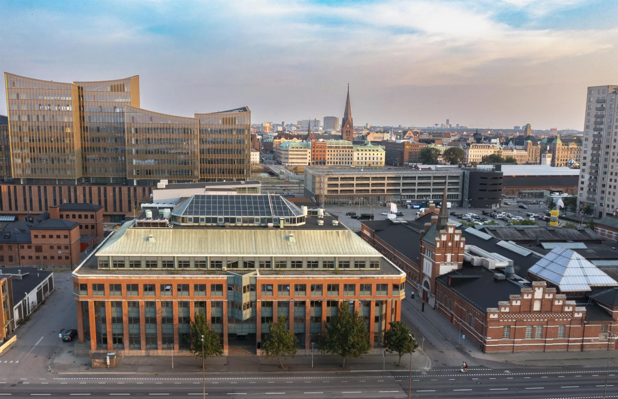 En stadsvy med byggnader, inklusive en tegelbyggnad med solpaneler på taket, och en kyrkspira i bakgrunden.