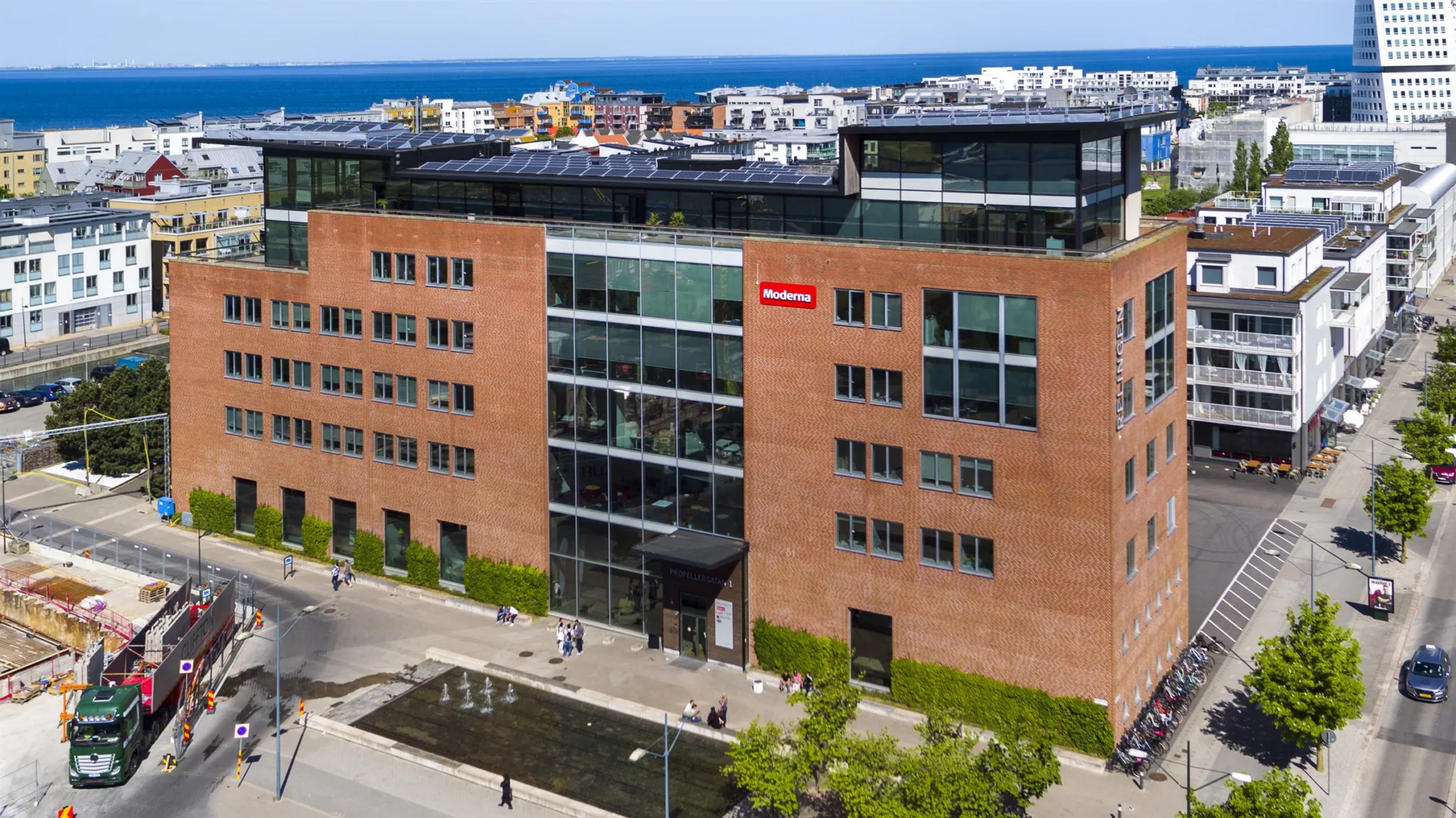 Alla bilder visar en modern byggnad med röd tegelvägg, stora glaspartier i mitten och en skylt med texten "Malmö universitet". I förgrunden syns en liten park med gångvägar och en fontän.