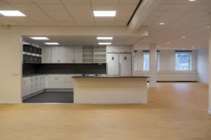 Ett kök med vita skåp, svart bänkskiva och öppet utrymme med ljust trägolv.