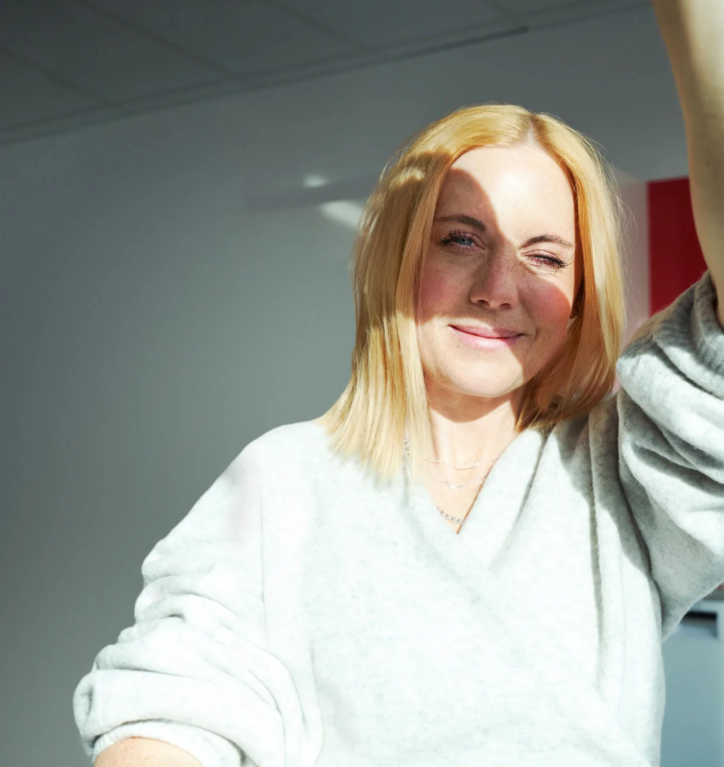 5. En kvinna med ljust hår som står i solljus och ler mot kameran.