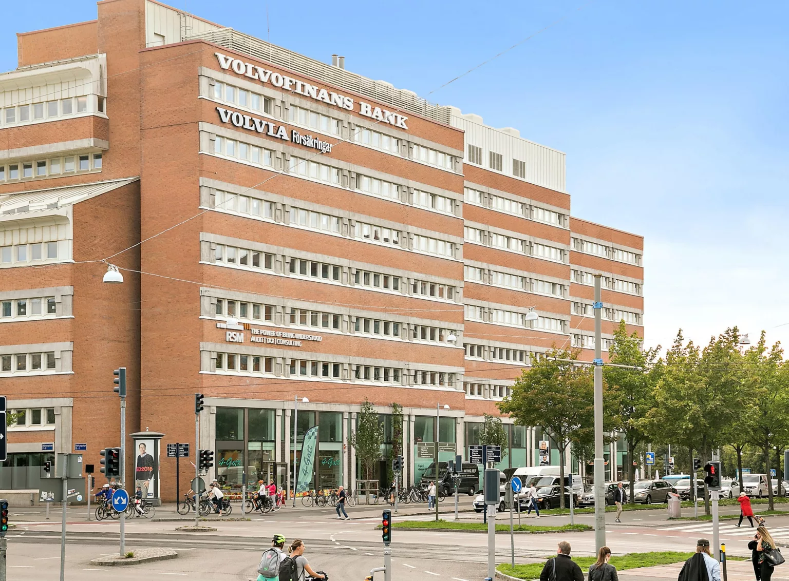1. En stor tegelbyggnad med flera våningar, texten "Vasaterminalen Gatuplan" syns högst upp, omgiven av träd och fotgängare.