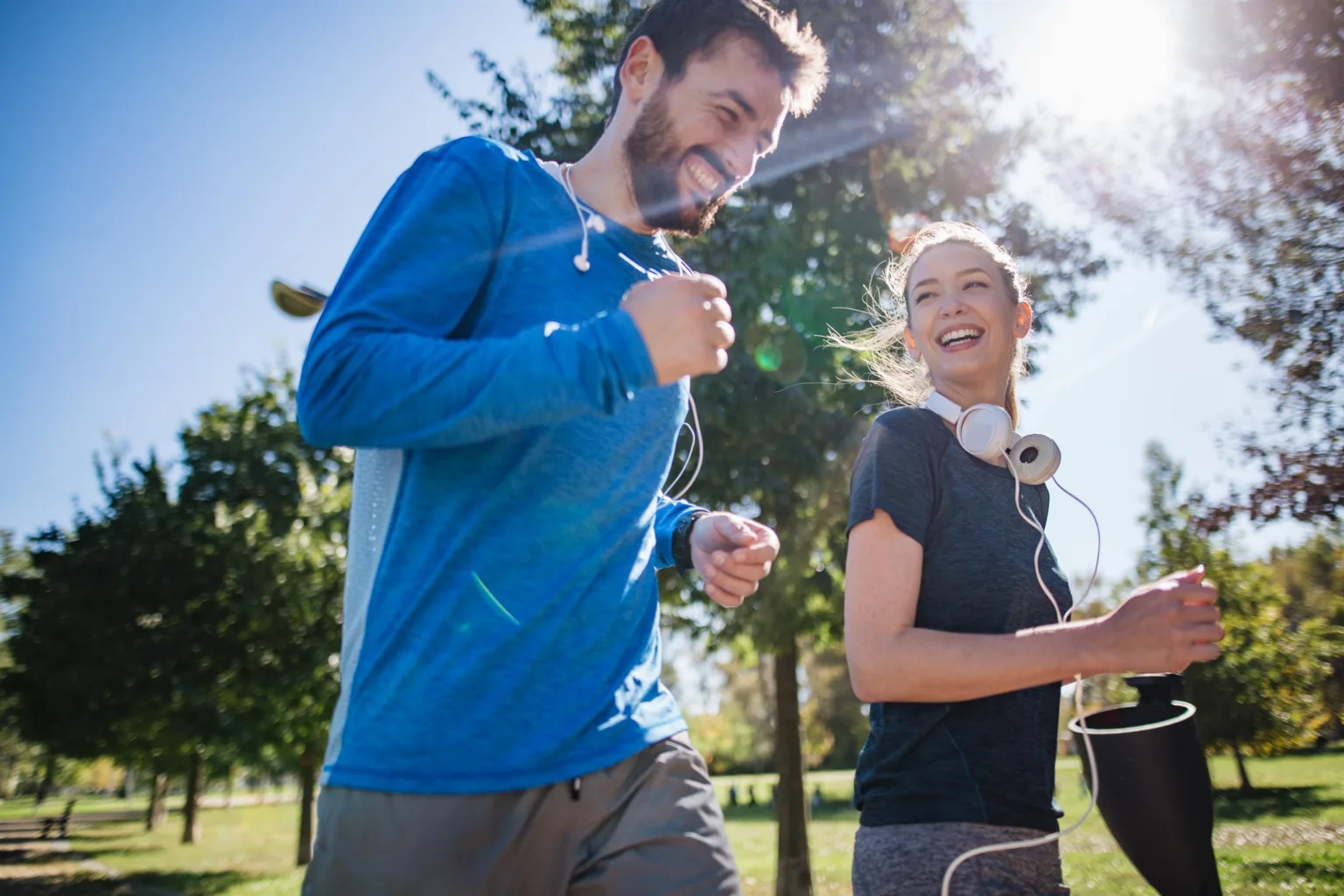 En man och en kvinna joggar tillsammans utomhus i soligt väder, båda ler.