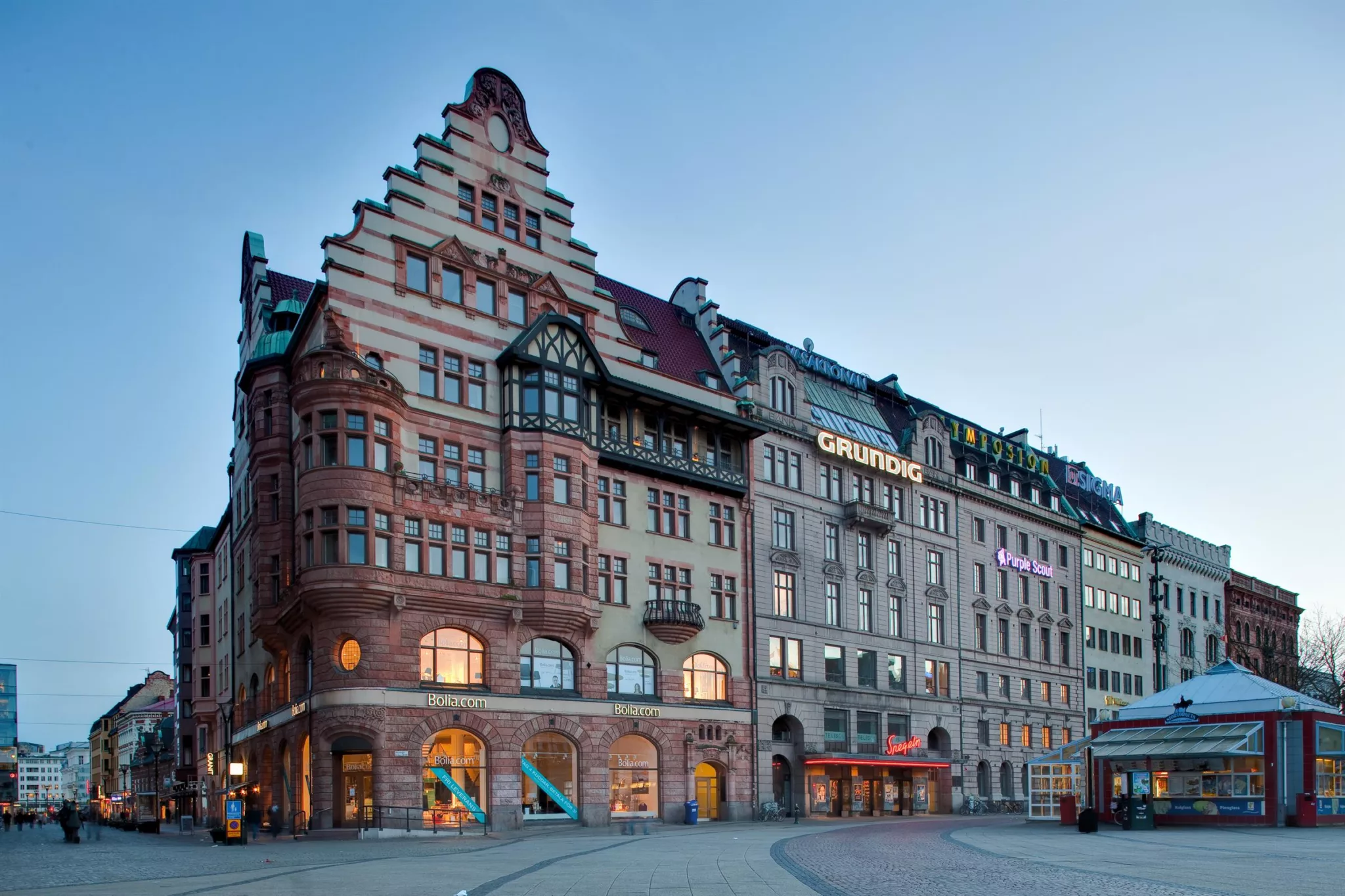 3. En större byggnad med trappstegsformad takfasad och detaljerade fönster, omgiven av stadsmiljö.