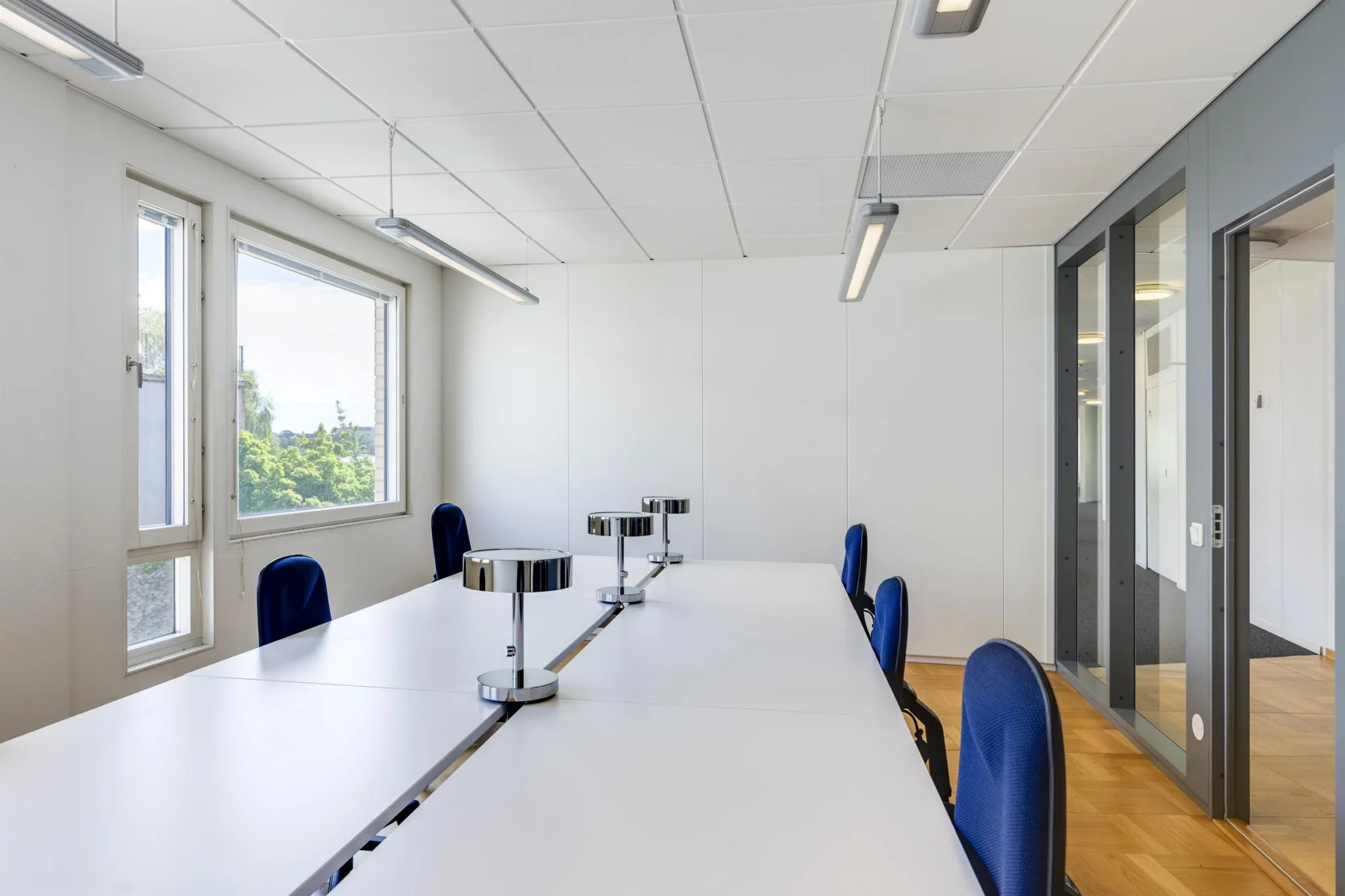 3. Ett konferensrum med ett långt vitt bord, blå stolar och stora fönster som släpper in dagsljus.