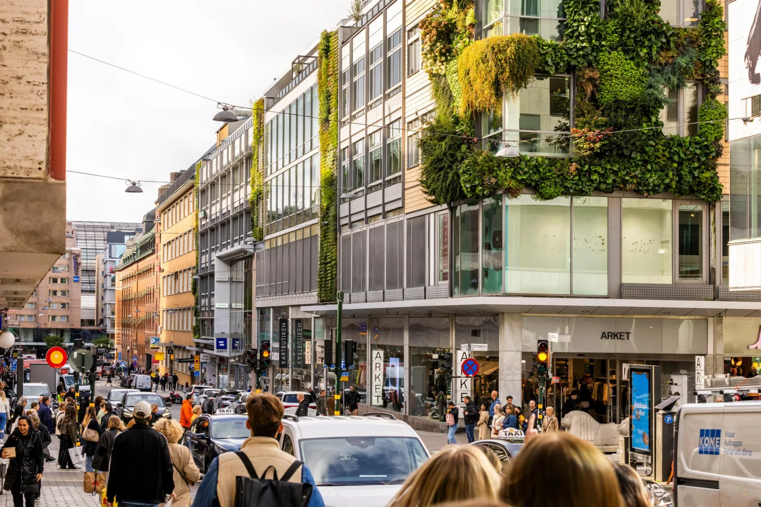 En stadsgata med människor, bilar och en byggnad med grön växtvägg.