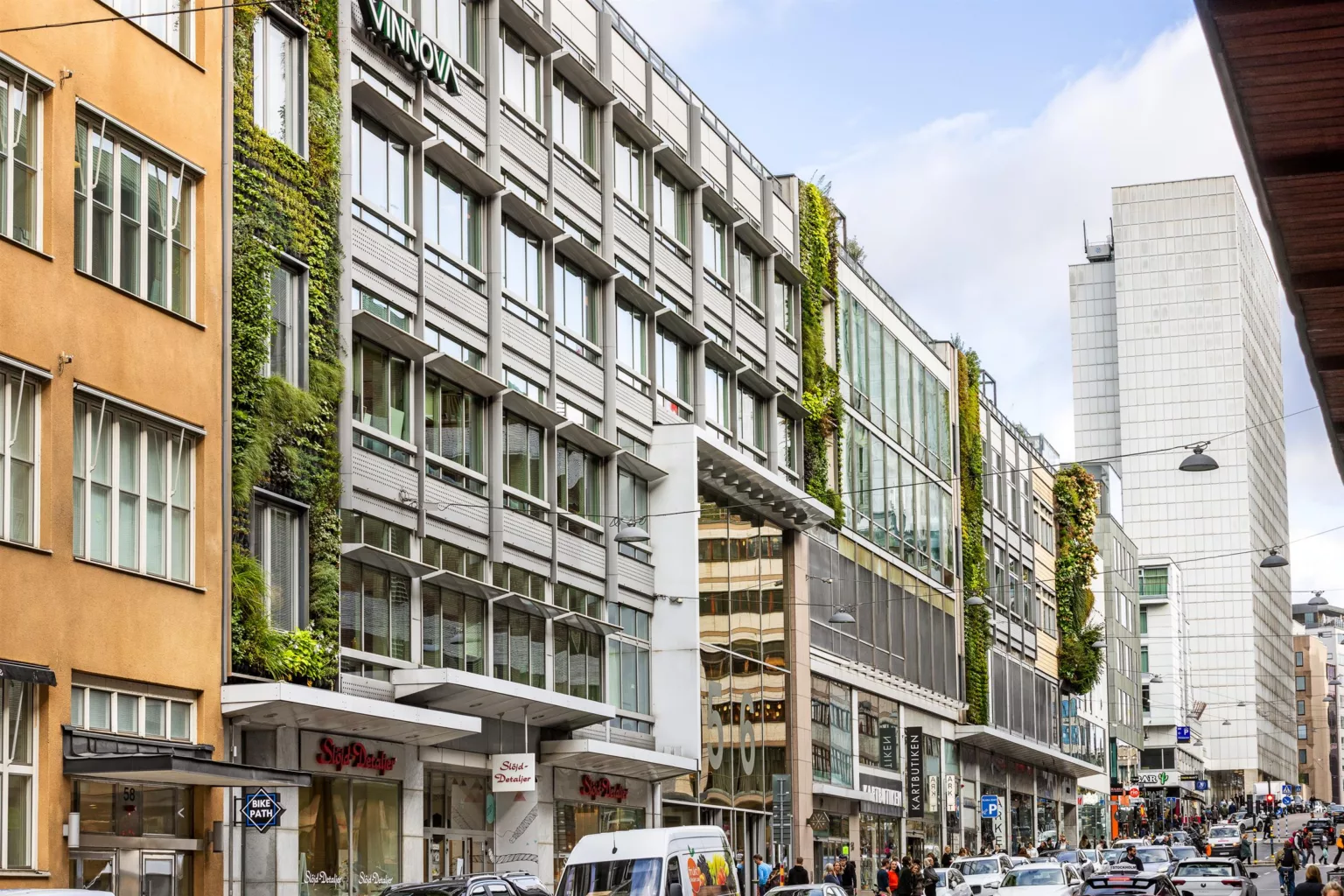 2. En rad byggnader med glasfönster och växtbeklädda fasader längs en stadsgata.