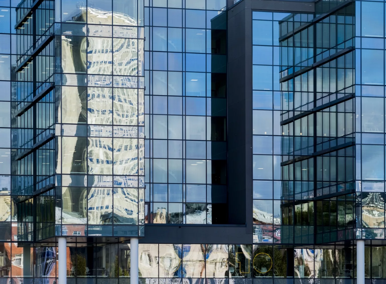 Reflektioner av omgivande byggnader i en glasfasad på en modern kontorsbyggnad.