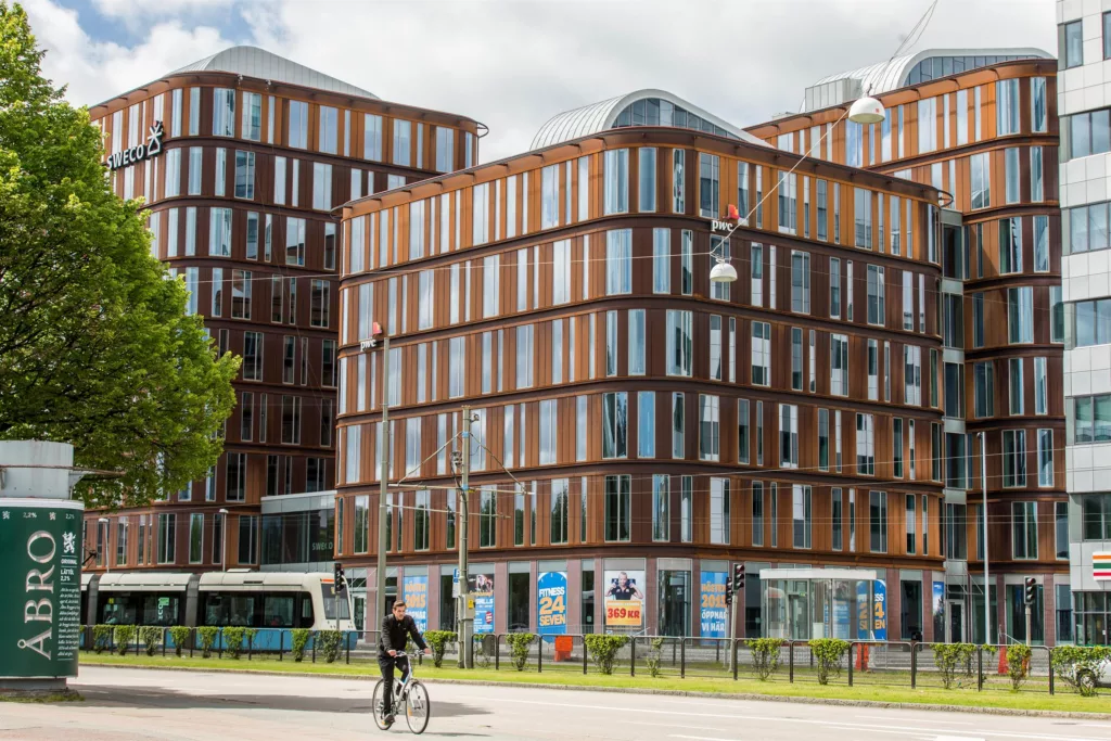 Flera byggnader med träfasader och glasfönster, en cyklist och en spårvagn syns i förgrunden.