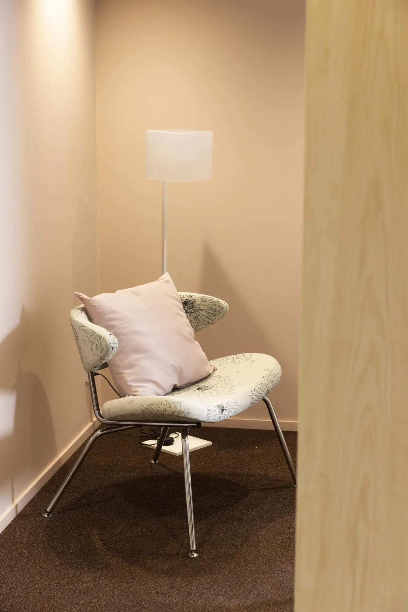 5. En mysig hörna med en beige fåtölj, en rosa kudde och en golvlampa i ett dämpat upplyst rum.