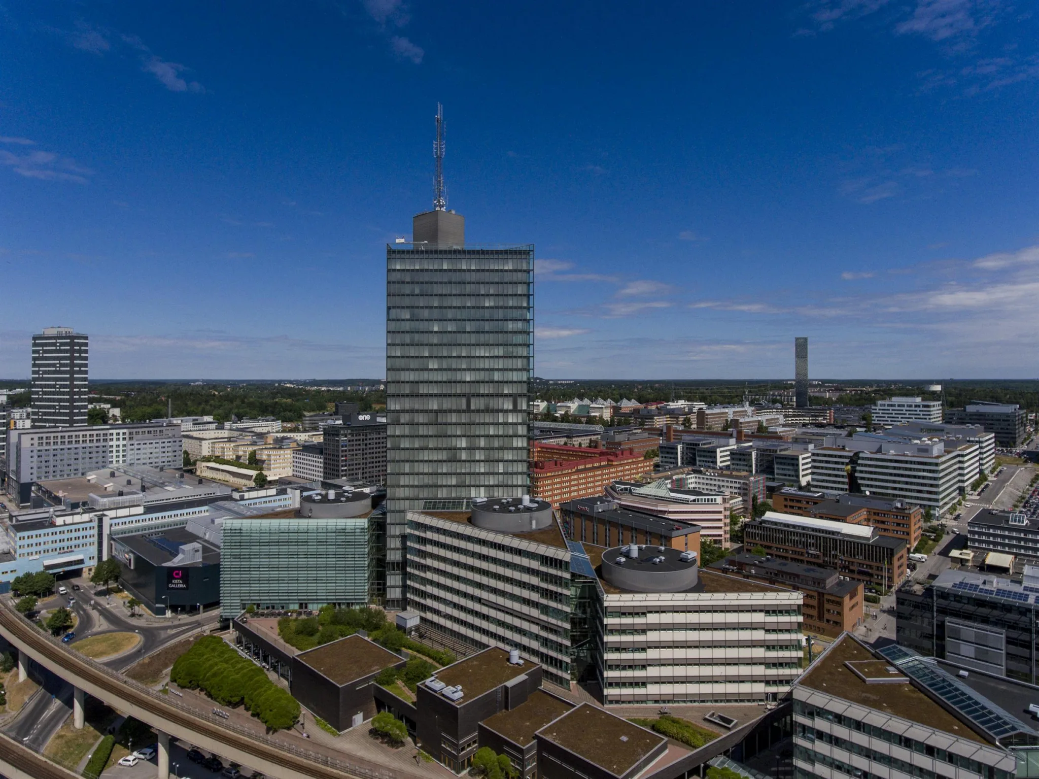 1. En stadsvy med en hög byggnad i centrum och flera mindre byggnader runtom under en klarblå himmel.