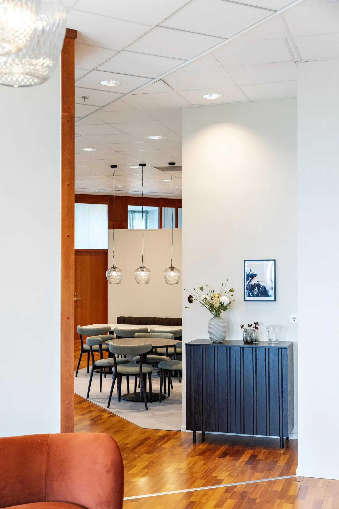 5. Stilren interiör med bord och stolar i en ljus matsal och en mörk skänk med blommor i förgrunden.
