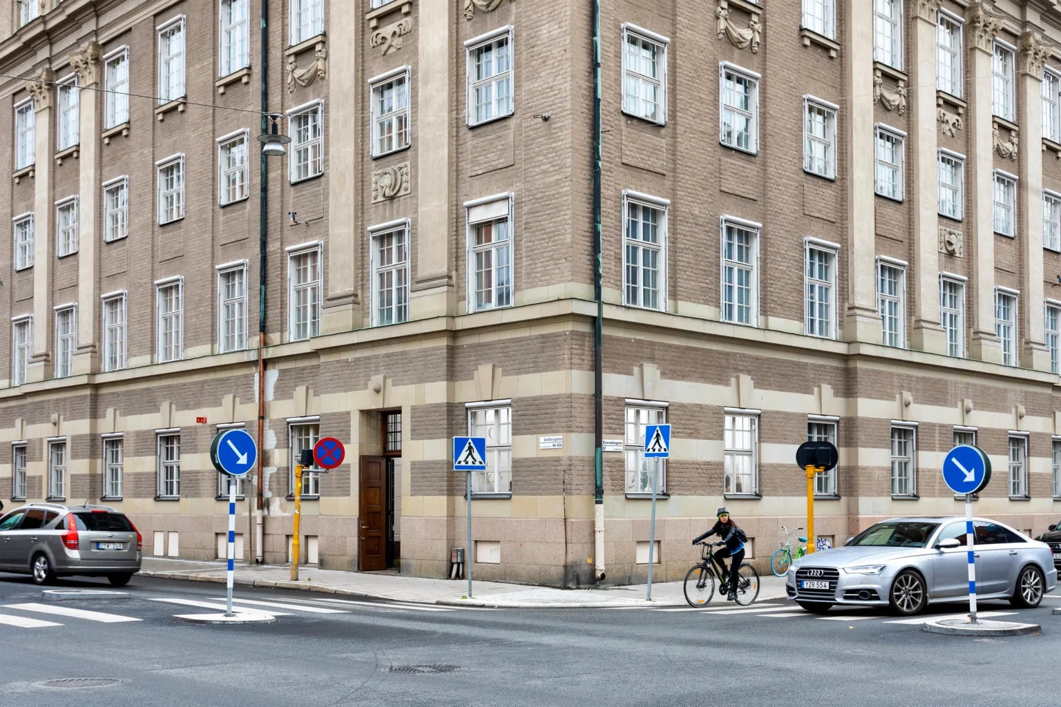 En hörnbyggnad i tegel med flera fönster och cyklist på gatan framför.