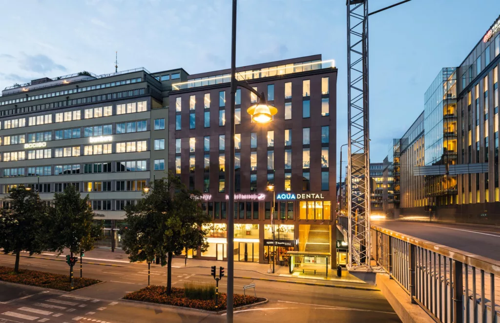 Modern byggnad med stora fönster och upplysta skyltar, kvällstid.