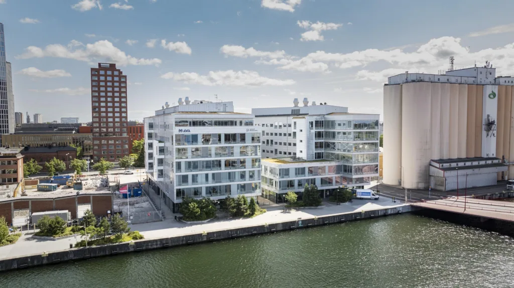 Vita moderna byggnader vid en kanal med träd och blå himmel.