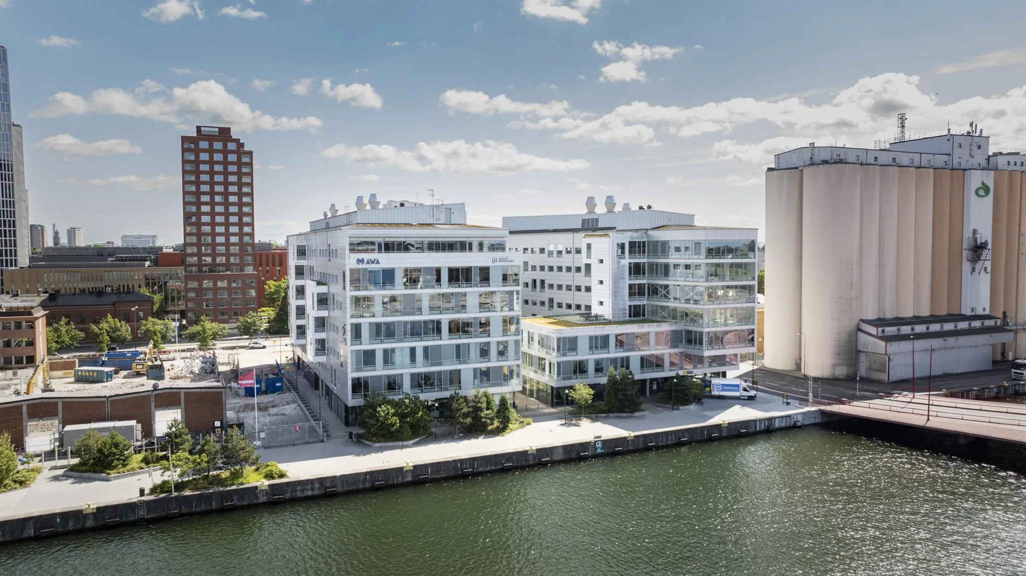 Vita moderna byggnader vid en kanal med träd och blå himmel.