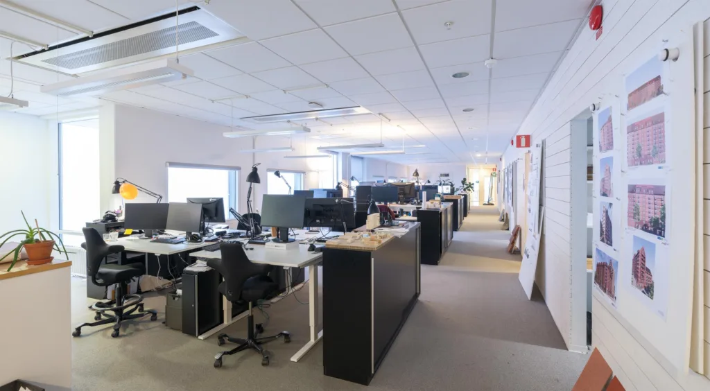 2. Ett öppet kontorslandskap med skrivbord, svarta stolar och datorer i en ljus och rymlig miljö.