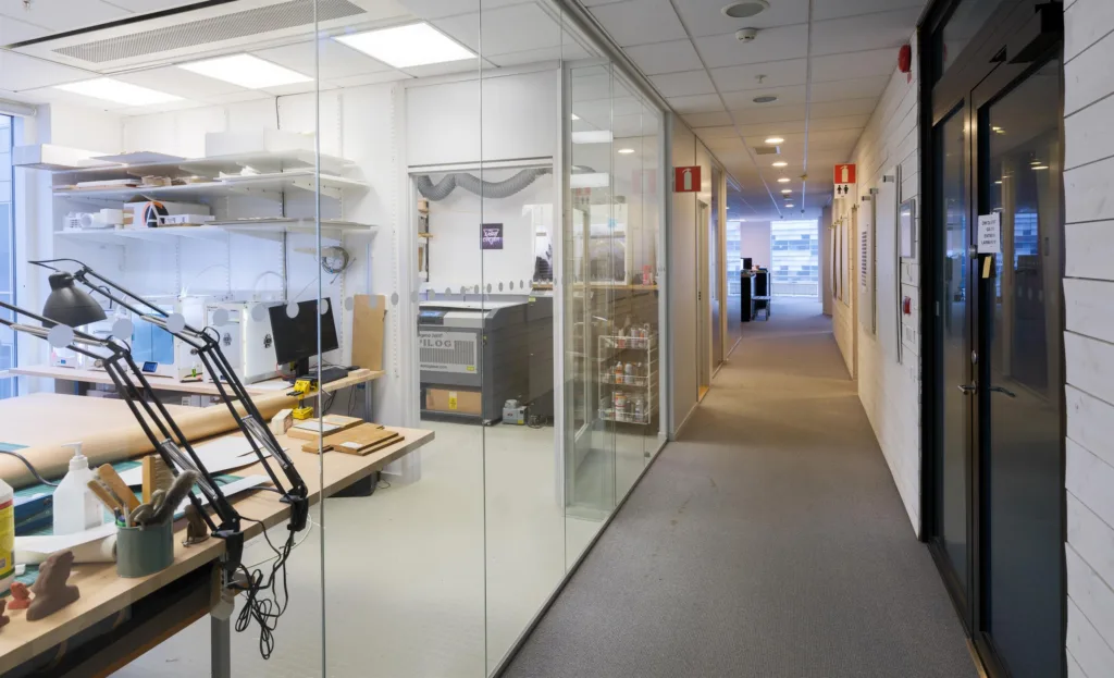 Kontorskorridor med glasväggar som visar arbetsplatser och kontorsutrustning.