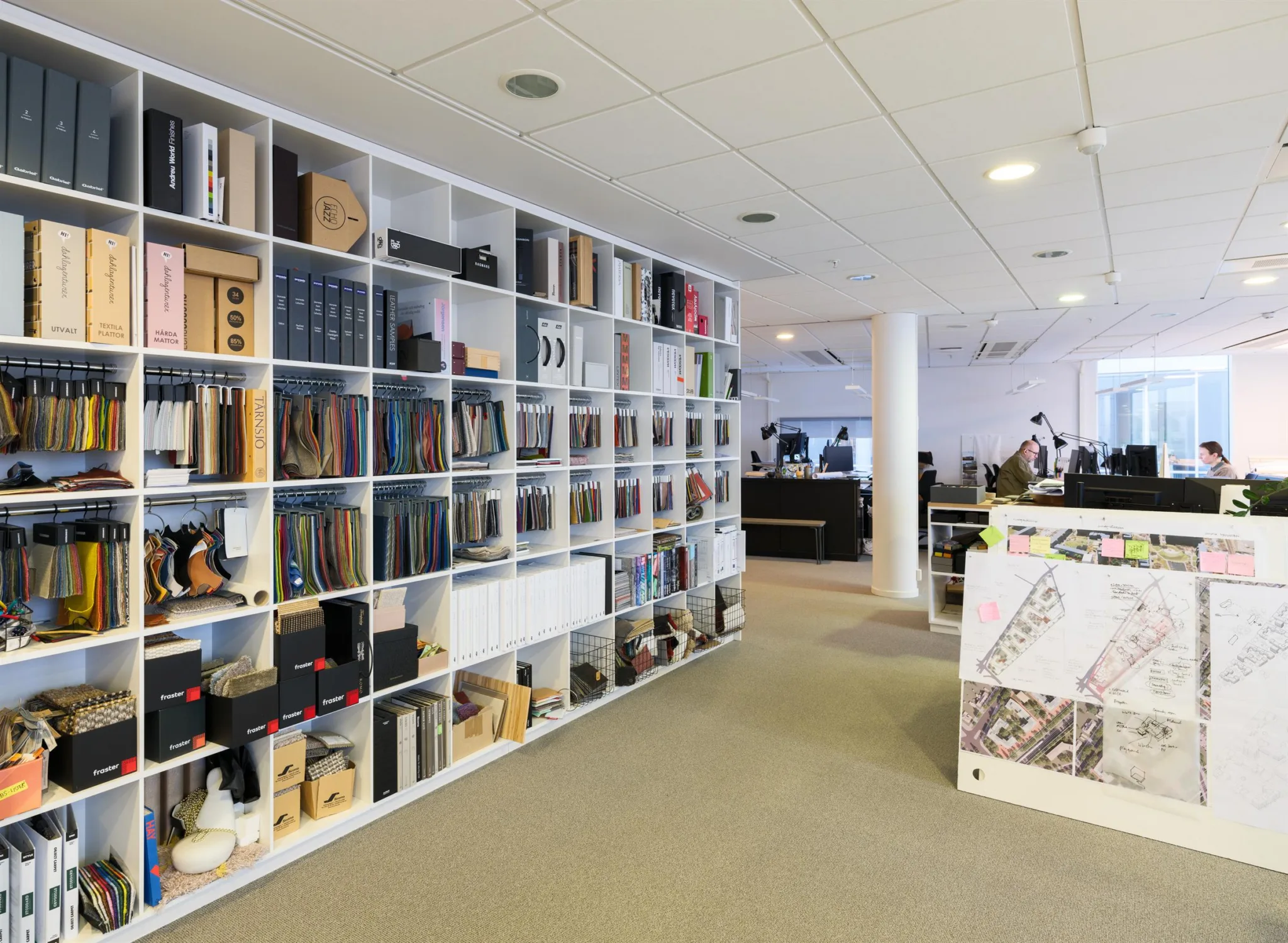 Ett kontor med en stor bokhylla fylld med böcker och föremål, samt arbetsstationer i bakgrunden.