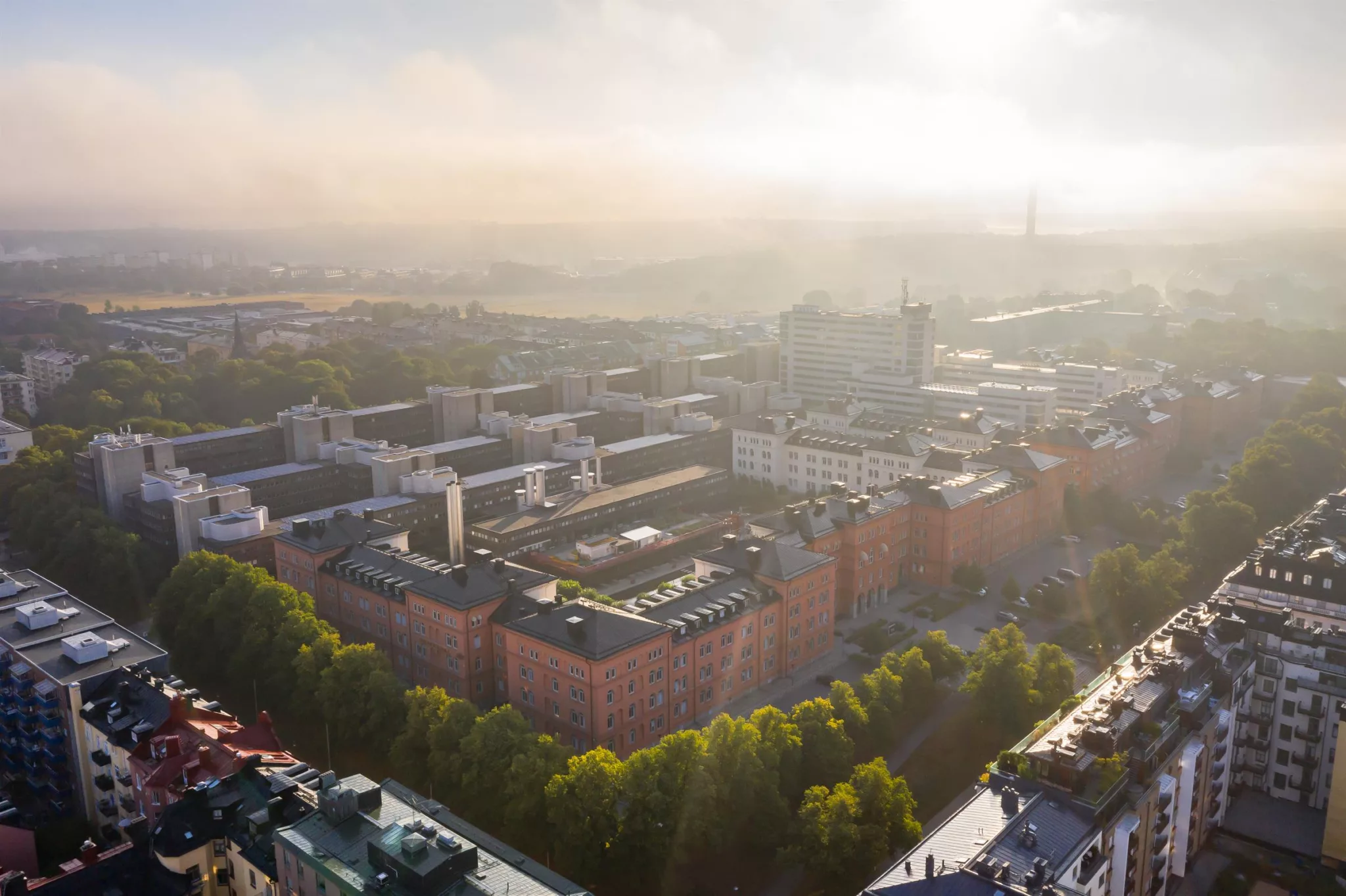 3. En fågelperspektivbild av en stadsdel med byggnader och grönska, täckt av mjukt solljus och dimma.