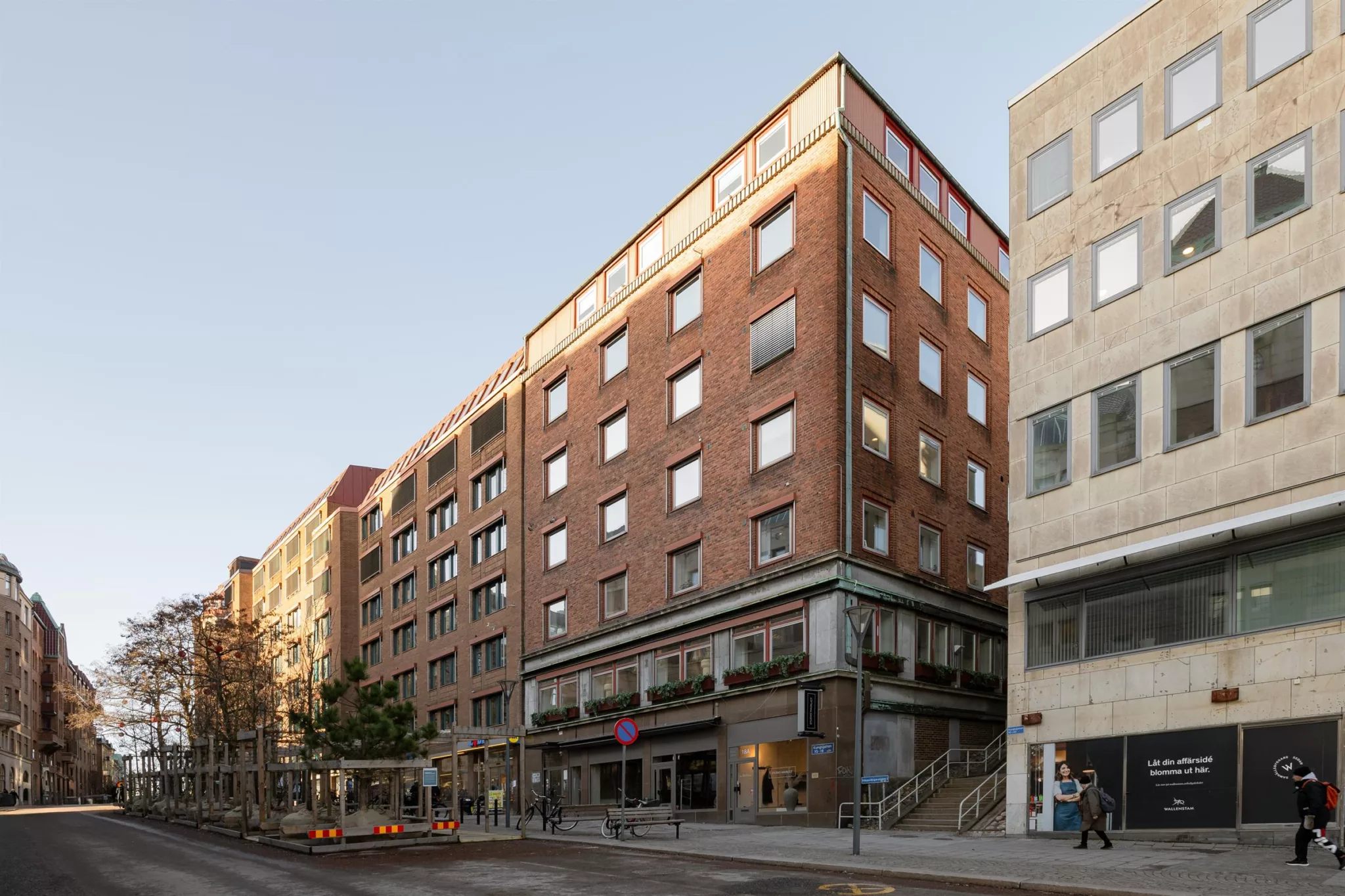 En flerbostadsbyggnad i röd tegel med flera våningar, butiker på bottenvåningen och närliggande gator.