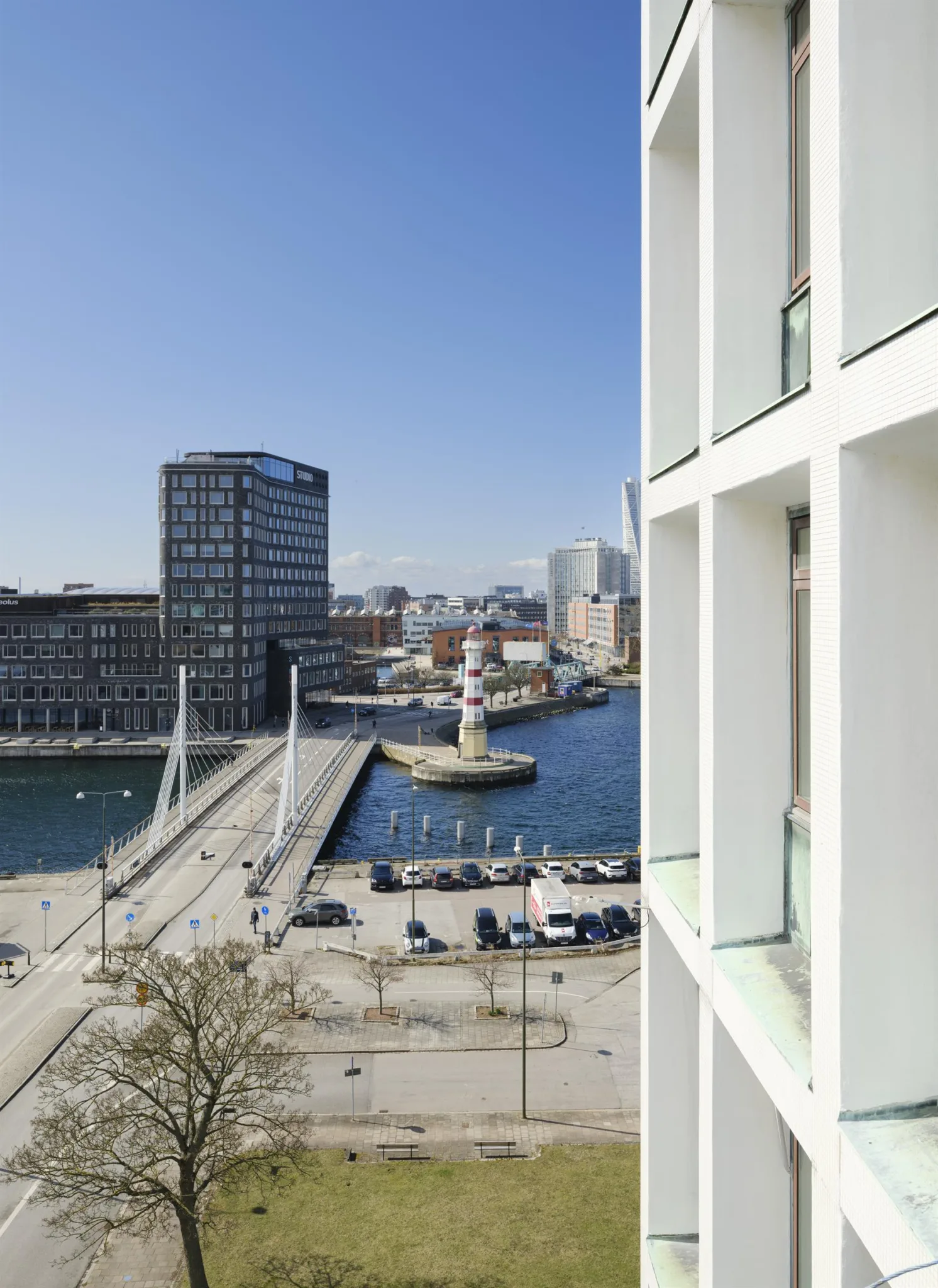 Vy från en byggnad som visar en modern stadsmiljö med bro, vatten och höghus under klarblå himmel.