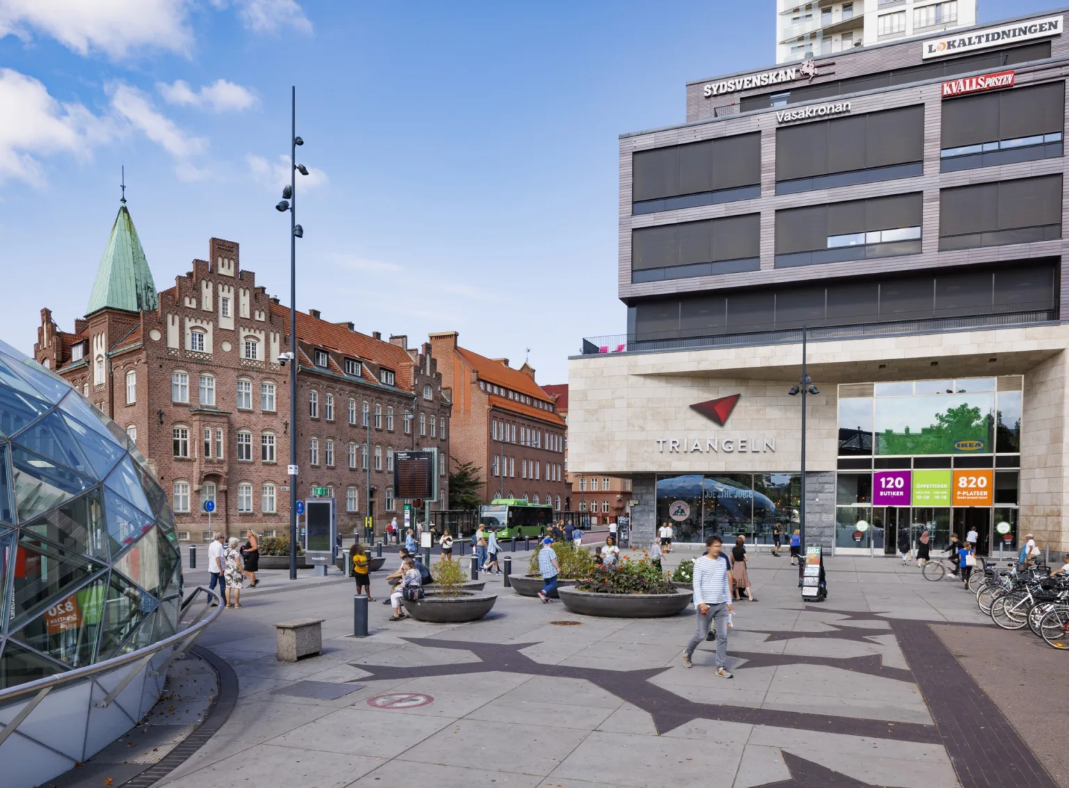 En stadsmiljö med moderna och historiska byggnader, människor som rör sig och cyklar.