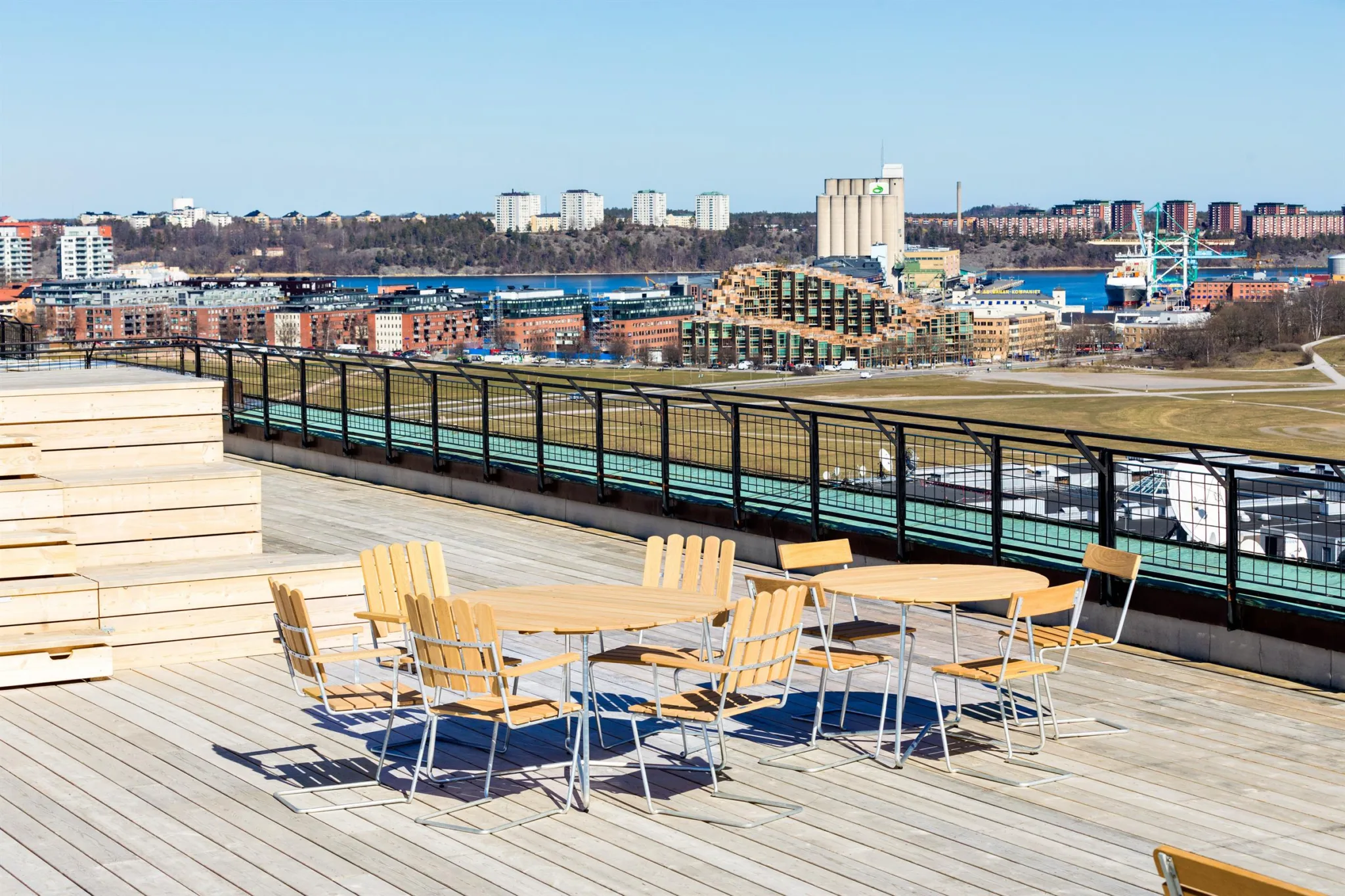 5. En takterrass med träbord och stolar, med utsikt över en stad och vatten.