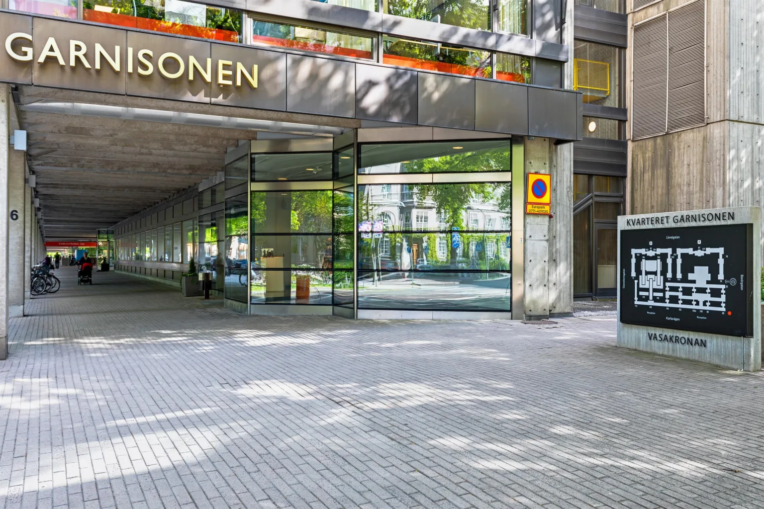 2. Entré till en byggnad med texten "KONSULEN" ovanför glasdörrar och grönska reflekterad i fönstren.