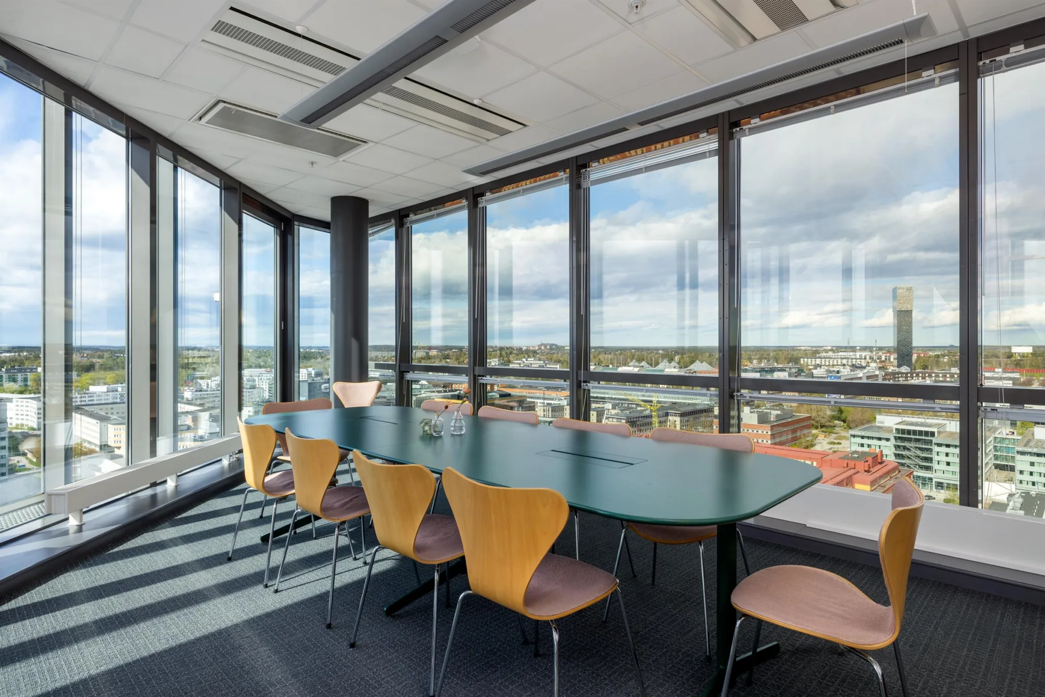 4. Ett konferensrum med ett långt mörkt bord, ljusa stolar och stora fönster som visar en vy över en stad.