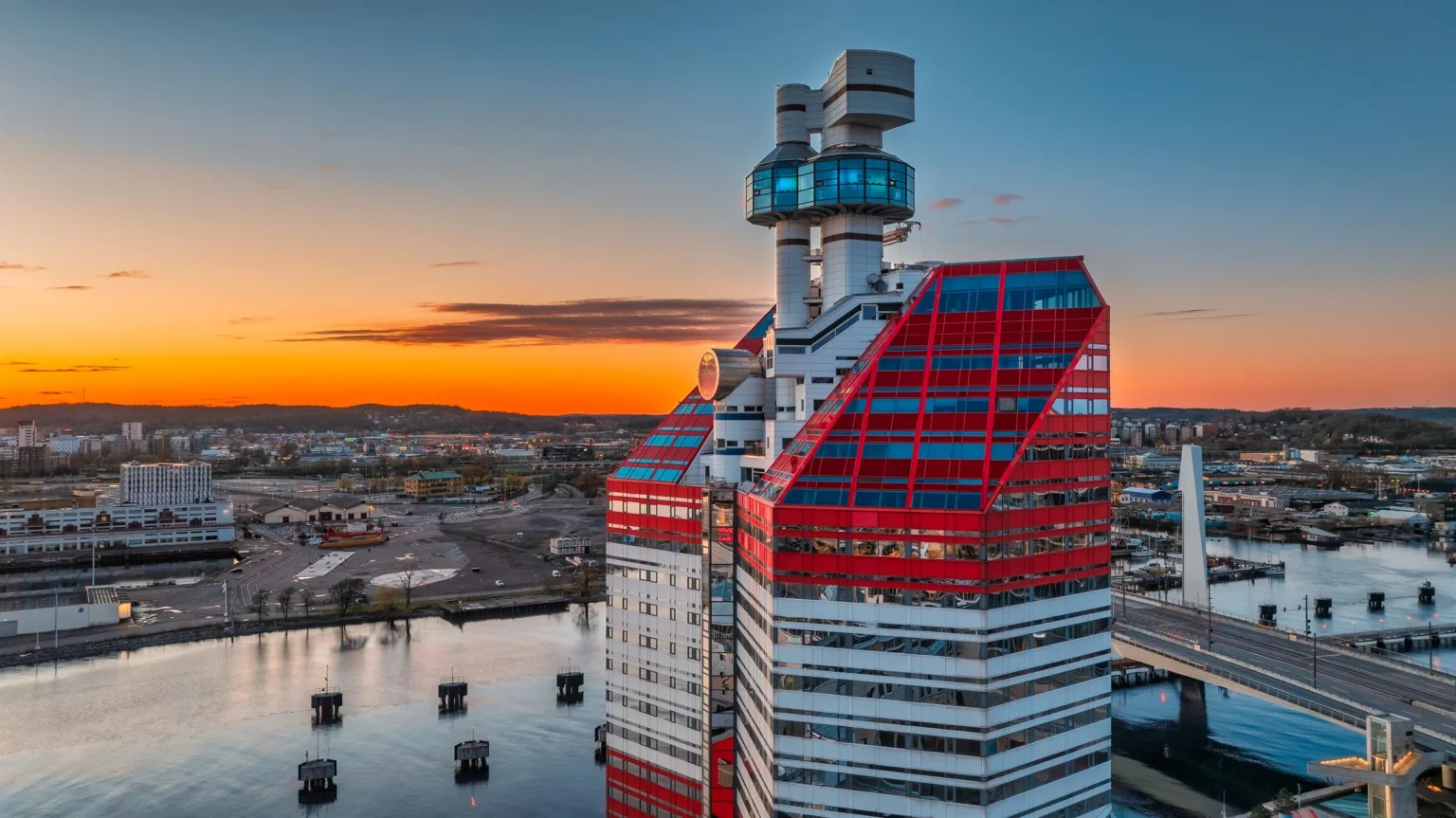 Modern byggnad med röd och vit fasad vid solnedgång nära vatten.