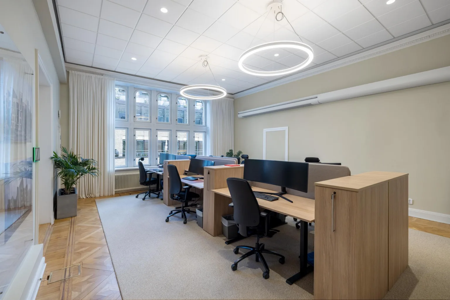 Modernt kontor med arbetsstationer, skrivbord, stolar och stora fönster som släpper in naturligt ljus.